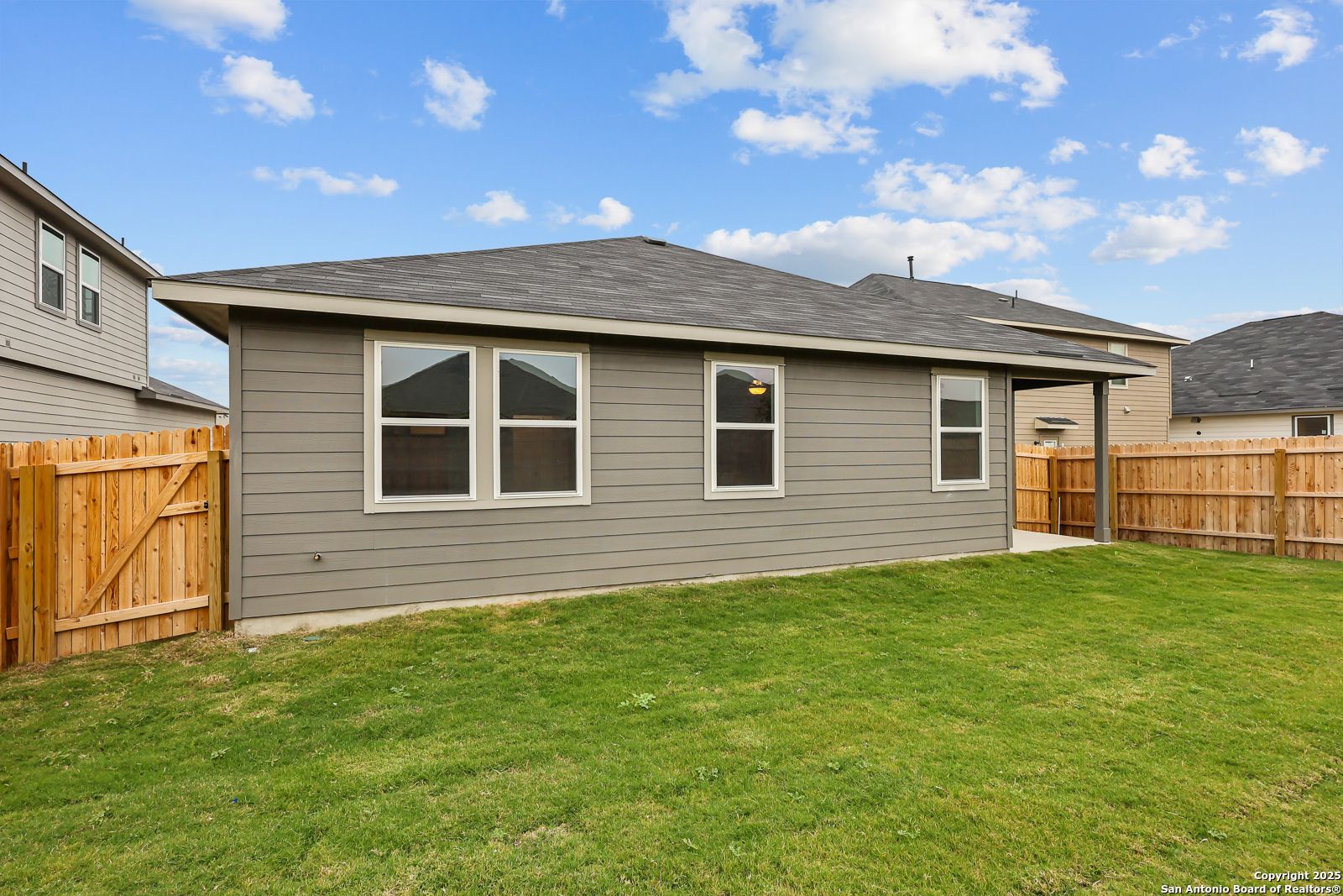 Gray single-story home exterior with large windows, covered patio, fenced backyard, and lush green lawn in Horizon Pointe, Converse, Texas