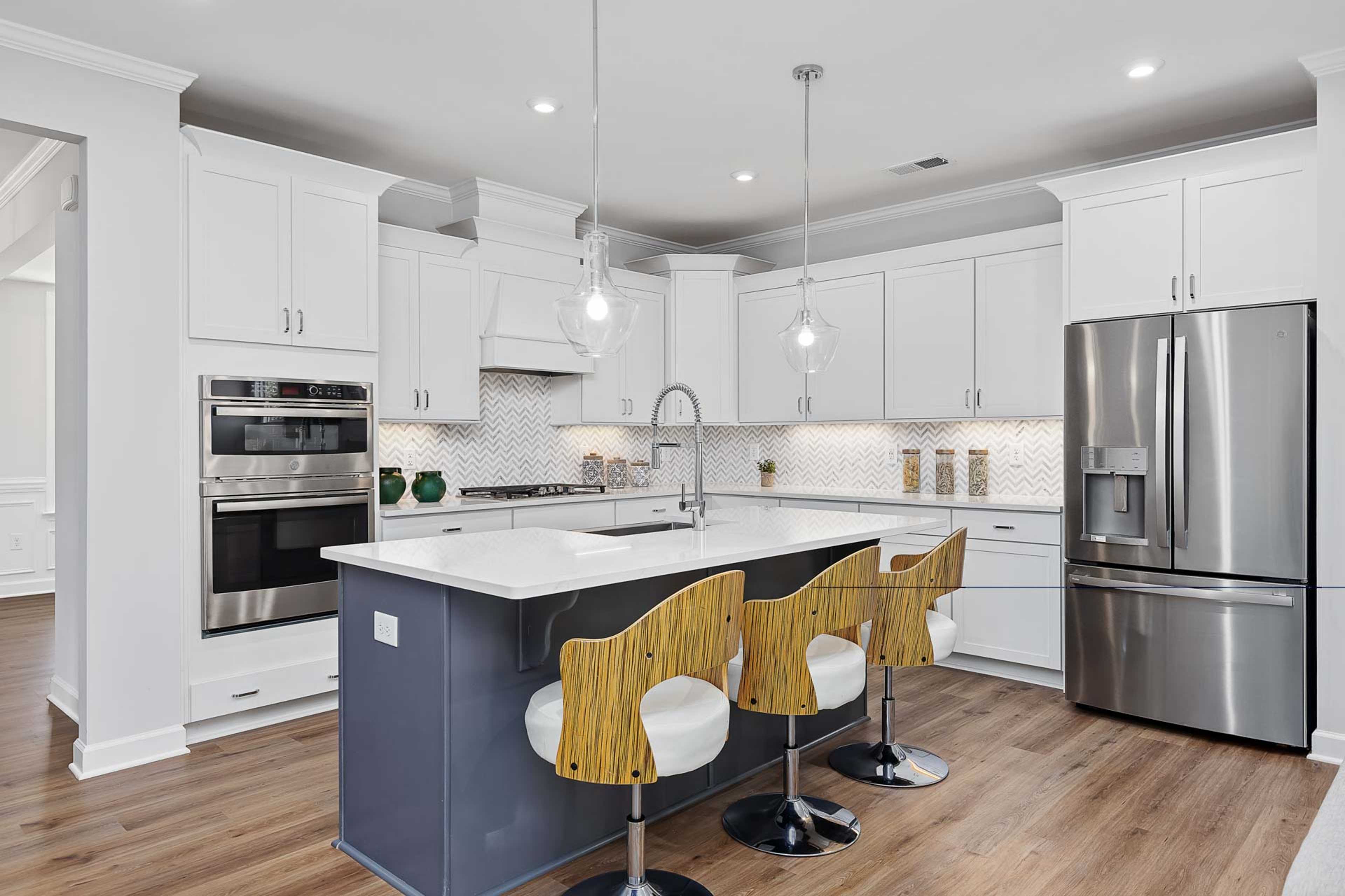 Modern kitchen in Glenmere Knightdale NC by Davidson Homes with white cabinets, navy island, bar stools, stainless appliances, hardwood floors