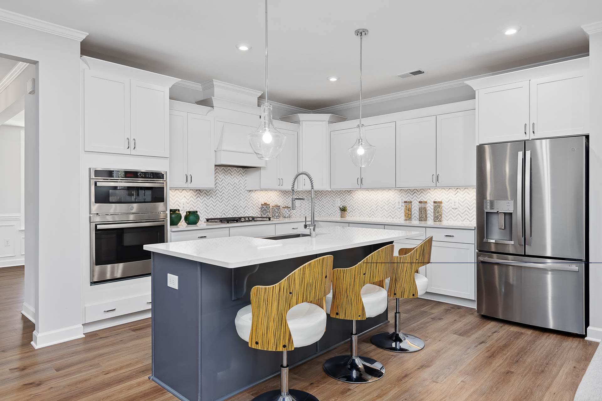 Modern kitchen in Glenmere Knightdale NC by Davidson Homes with white cabinets, navy island, bar stools, stainless appliances, hardwood floors
