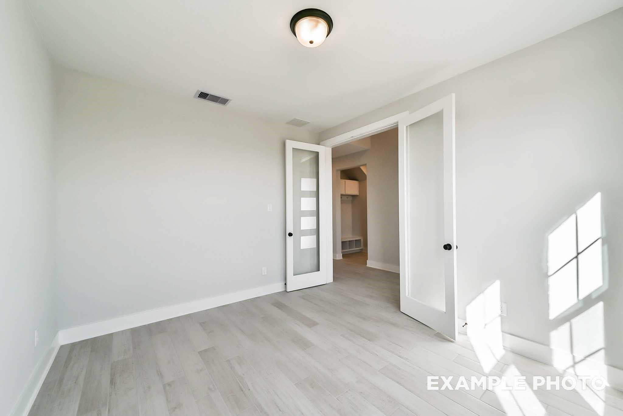 Bright bedroom featuring light gray walls, luxury vinyl plank flooring, and frosted glass double doors in Davidson Homes The Philip C, Rosharon, Texas