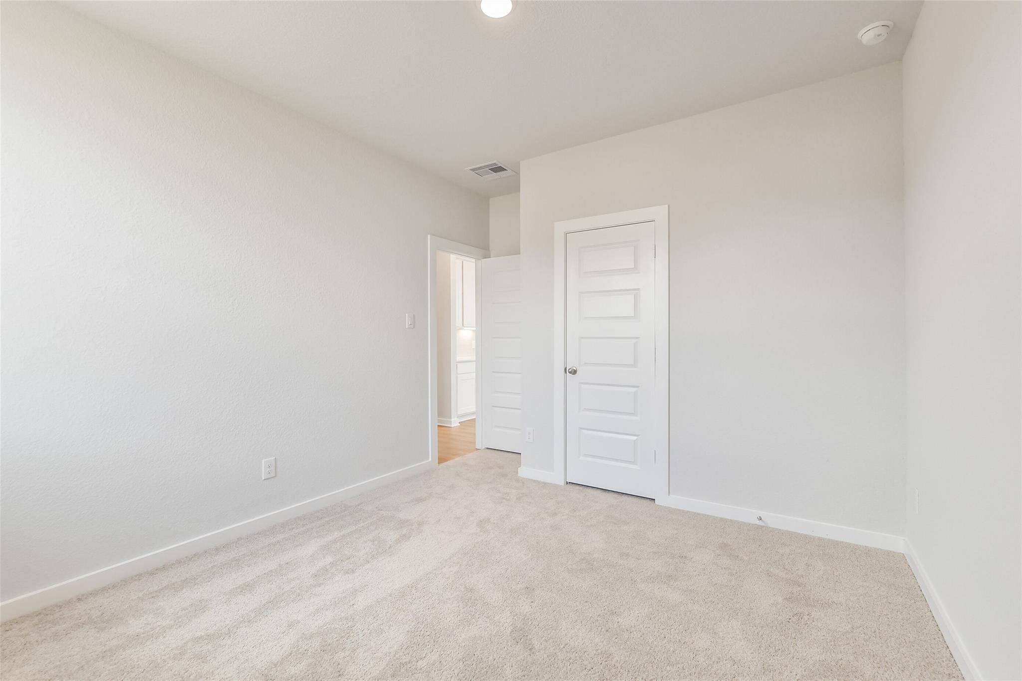 Empty secondary bedroom featuring beige carpet, white walls, closet door in Davidson Homes The Frio G, Cleveland, Texas