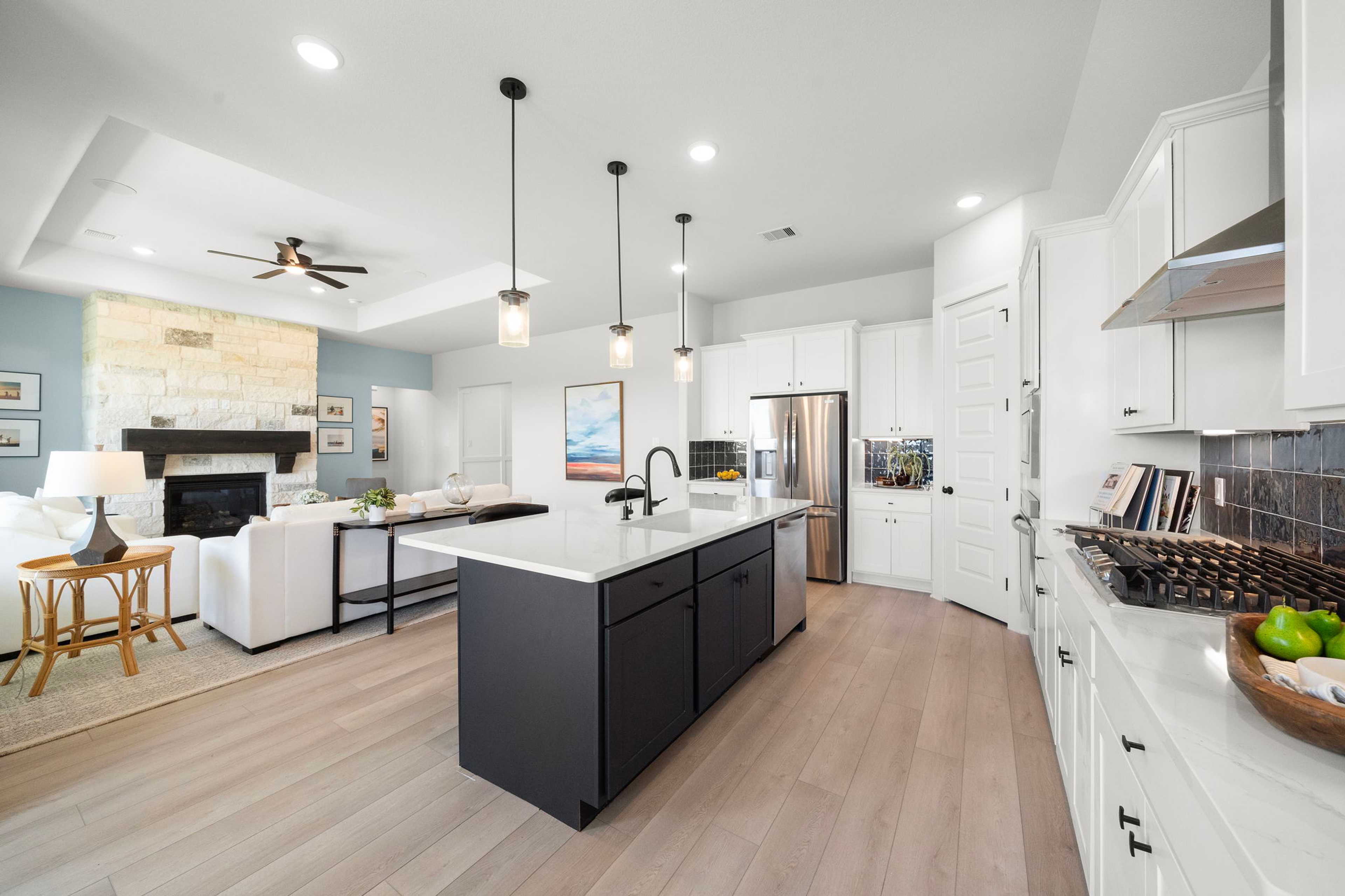 Open-concept kitchen and living area in Lago Mar home by Davidson Homes in Texas City, Texas with white cabinets, large island, stone fireplace, and hardwood floors
