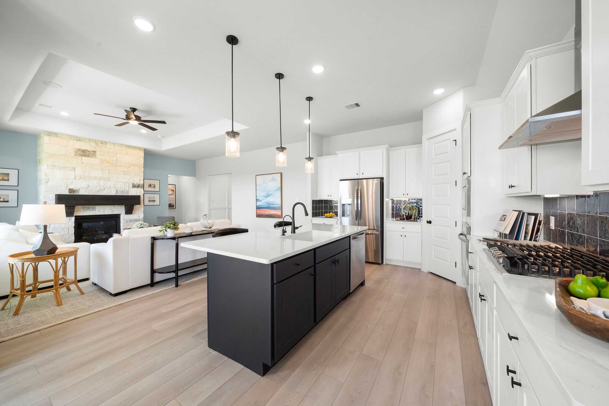 Open-concept kitchen and living area in Lago Mar home by Davidson Homes in Texas City, Texas with white cabinets, large island, stone fireplace, and hardwood floors