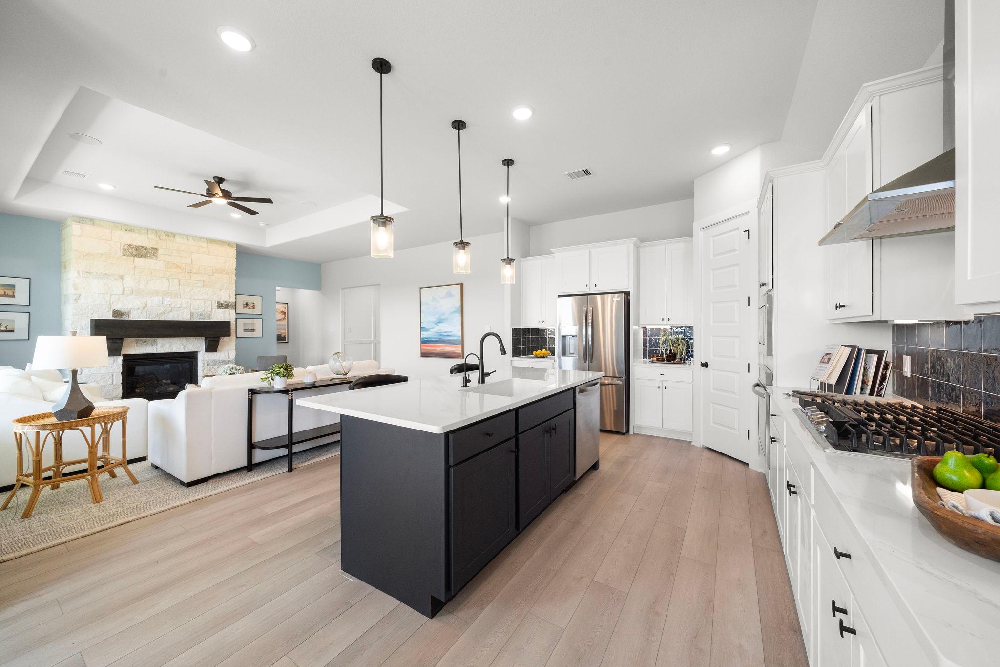 Open-concept kitchen and living area in Lago Mar home by Davidson Homes in Texas City, Texas with white cabinets, large island, stone fireplace, and hardwood floors