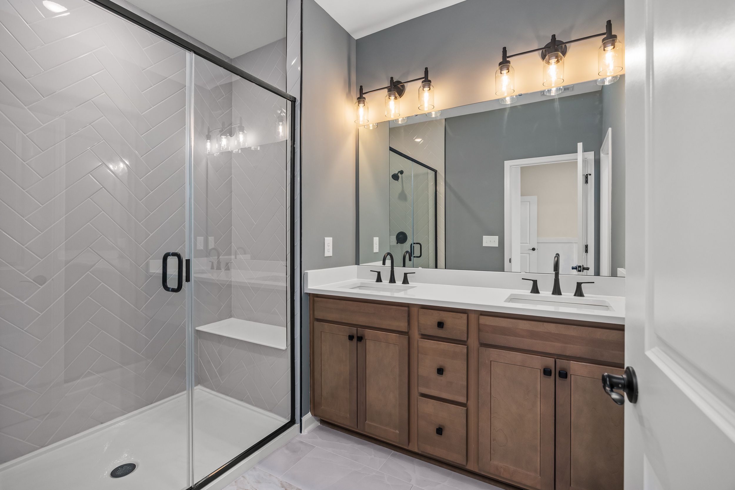 Spacious primary bathroom in Forestville Yard, Knightdale NC with frameless glass shower, gray subway tiles, and double shaker vanities