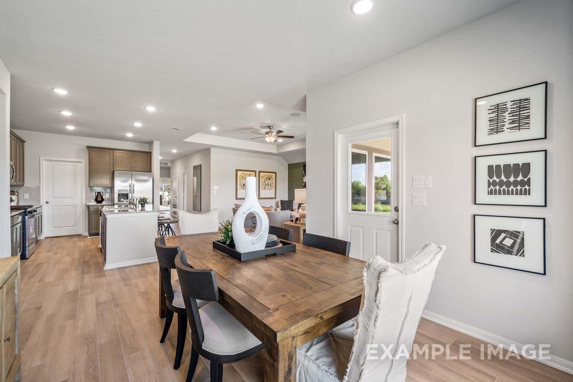 Modern open-concept dining area with wooden table, upholstered chairs, and potted plant beside sleek kitchen in Davidson Homes The Acadia A, Texas City