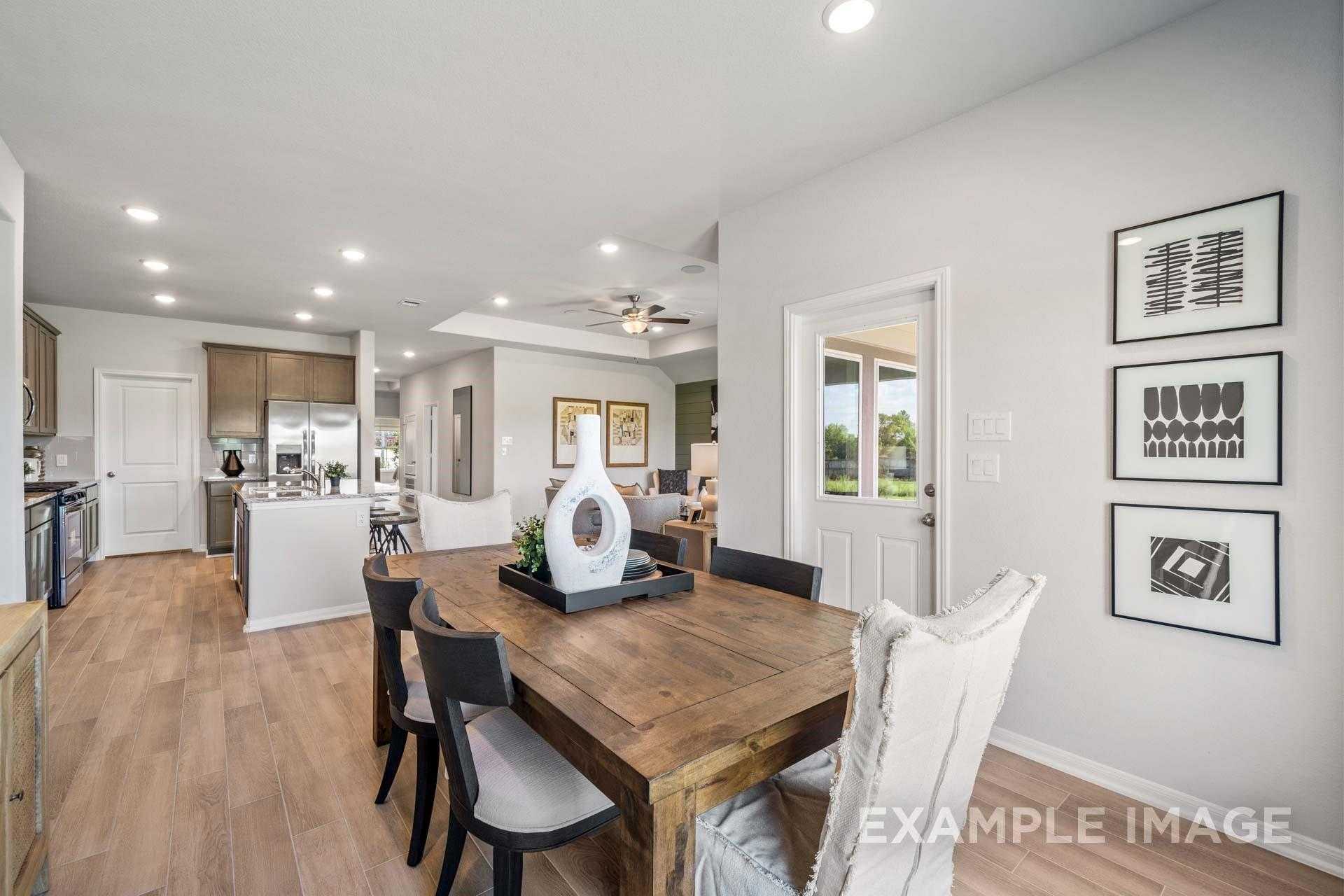Modern open-concept dining area with wooden table, upholstered chairs, and potted plant beside sleek kitchen in Davidson Homes The Acadia A, Texas City