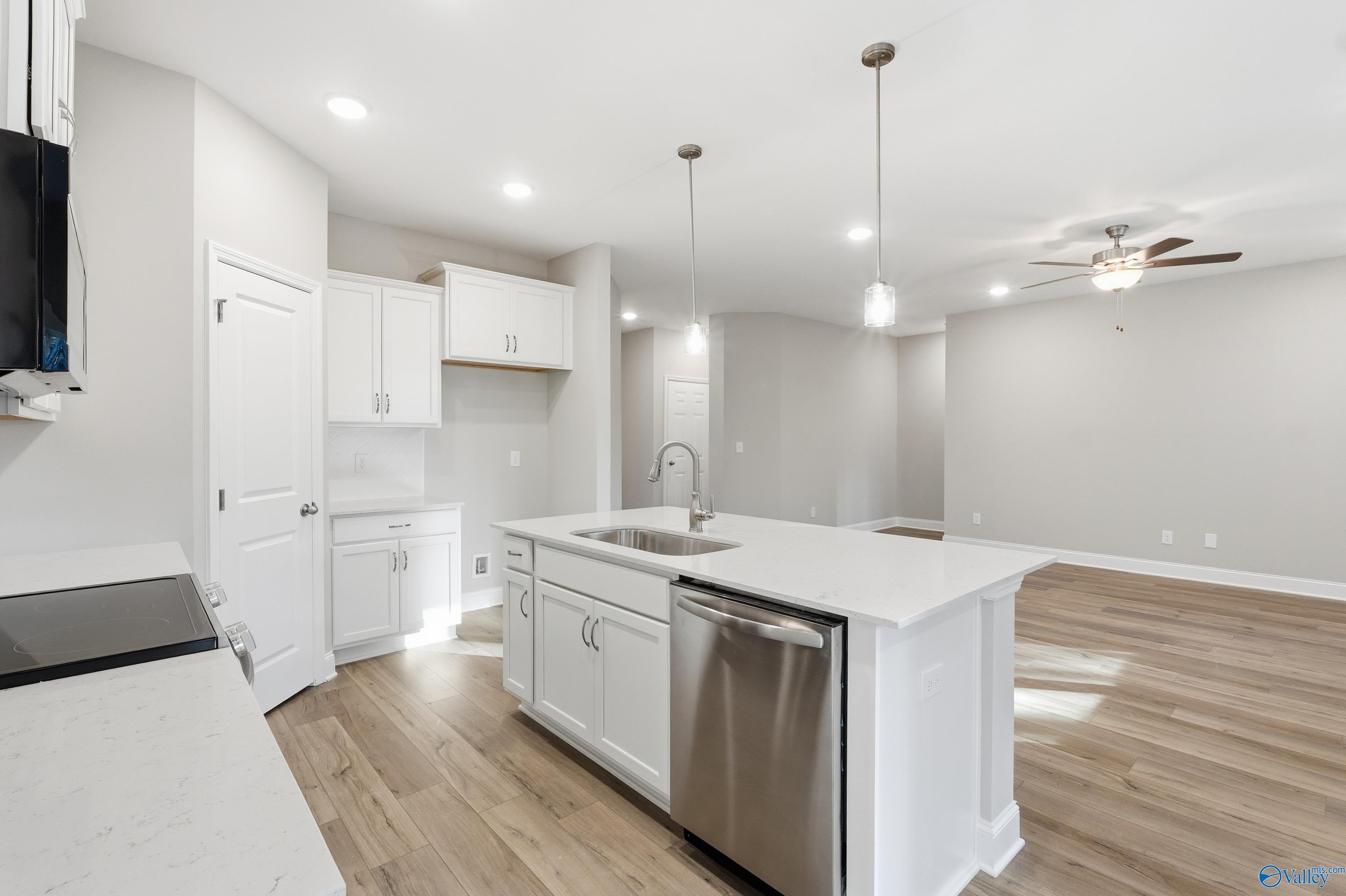 Modern white kitchen island with stainless sink and dishwasher, open to living area in The Asheville 3-bedroom home, Arab, Alabama