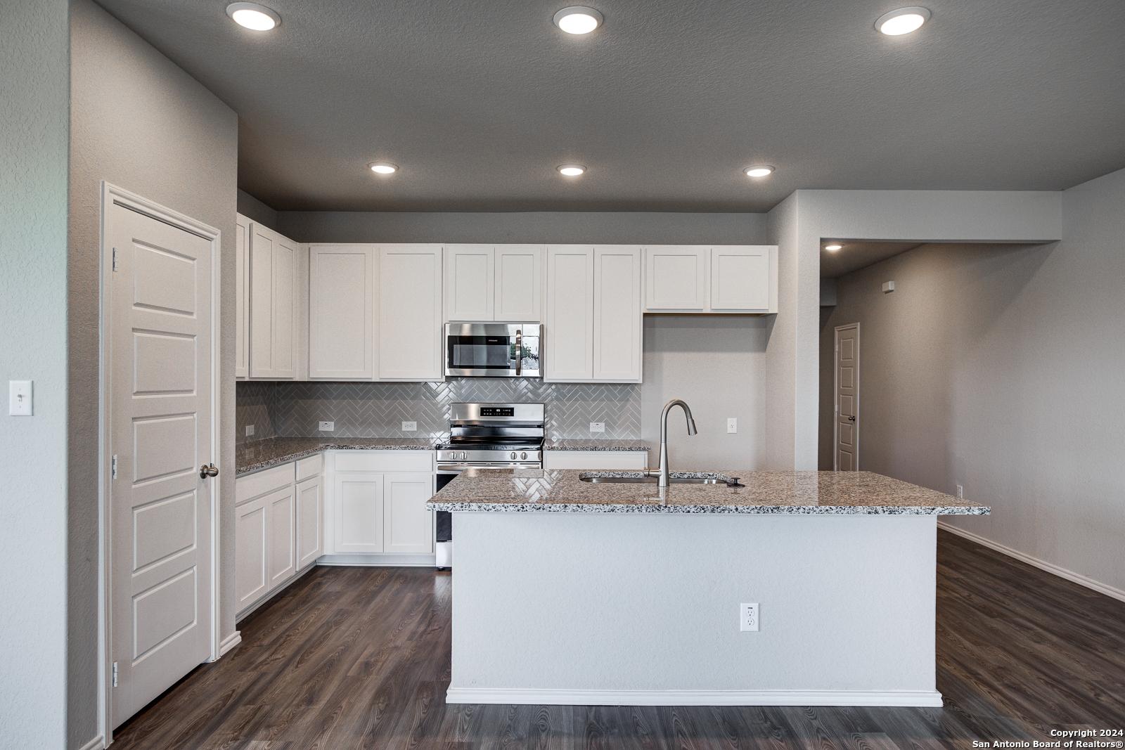 Modern open-concept kitchen with white cabinets, granite island sink, stainless appliances in The Daphne J, Seguin, Texas