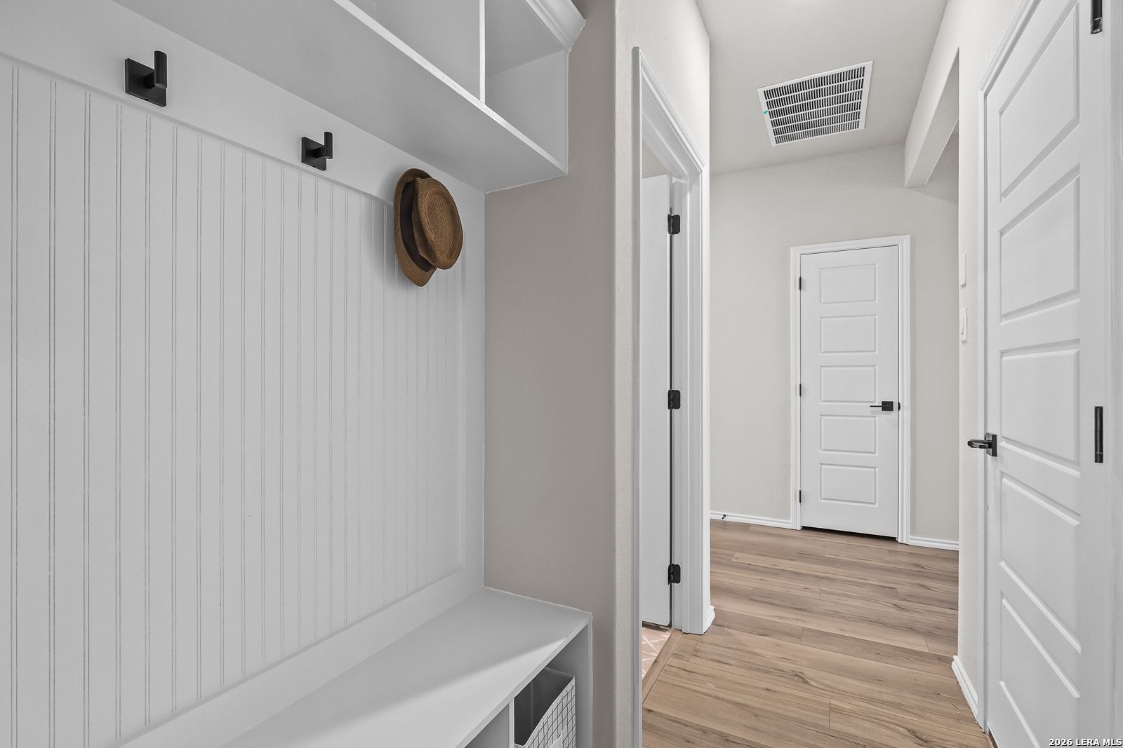 White mudroom bench with coat hooks and storage in The Daphne H floor plan at Hannah Heights, Seguin, Texas.