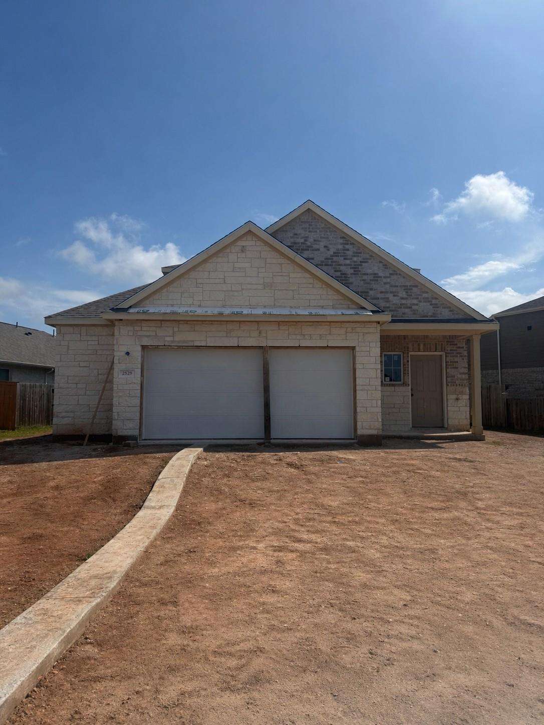 Modern two-story home with beige stone-brick facade, two-car garage, and dirt yard in Sunterra, Katy, Texas - Davidson Homes San Marcos H