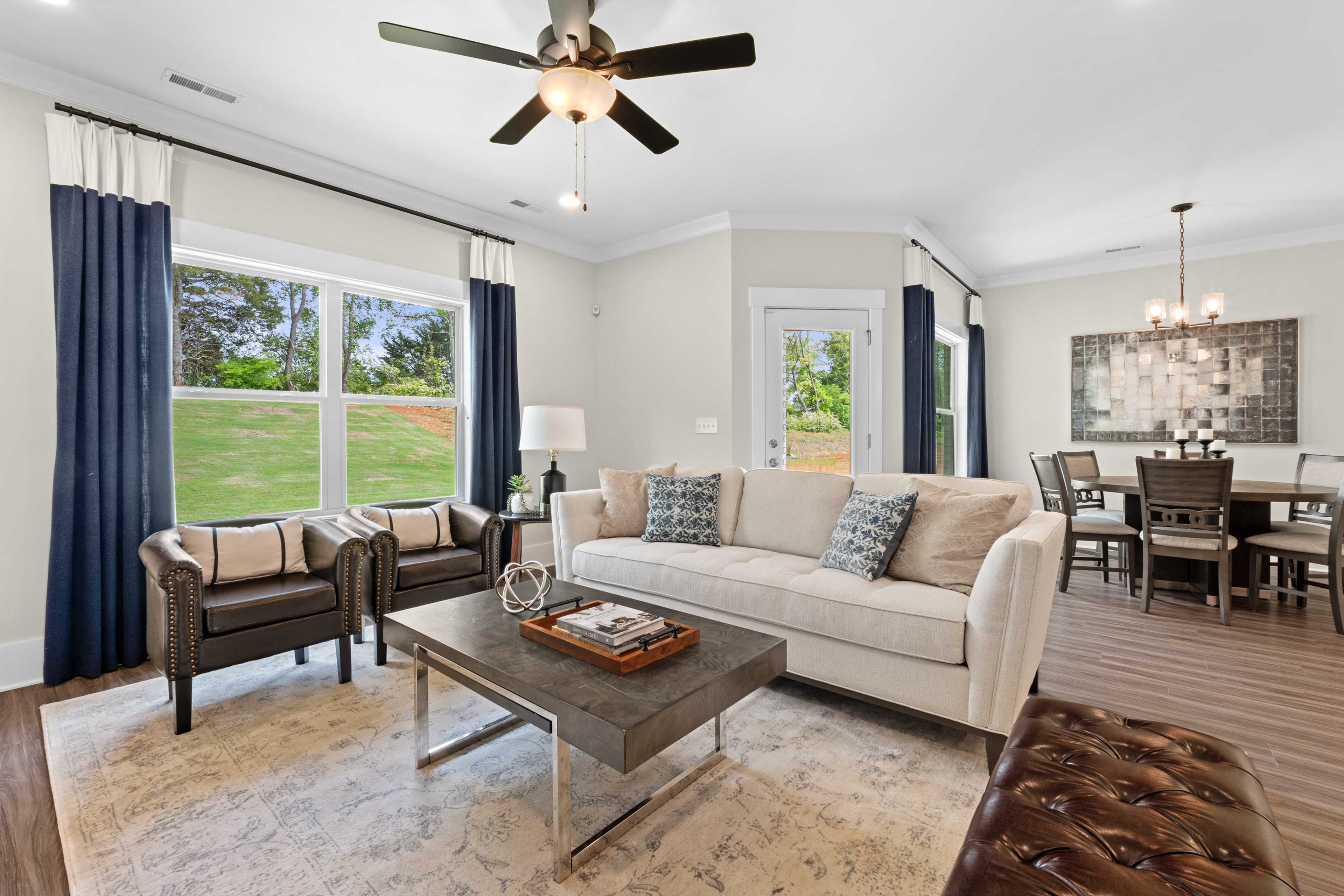 Spacious open-concept living and dining room at Ivy Hills in Toney Alabama with beige sectional sofa blue curtains hardwood floors and scenic views