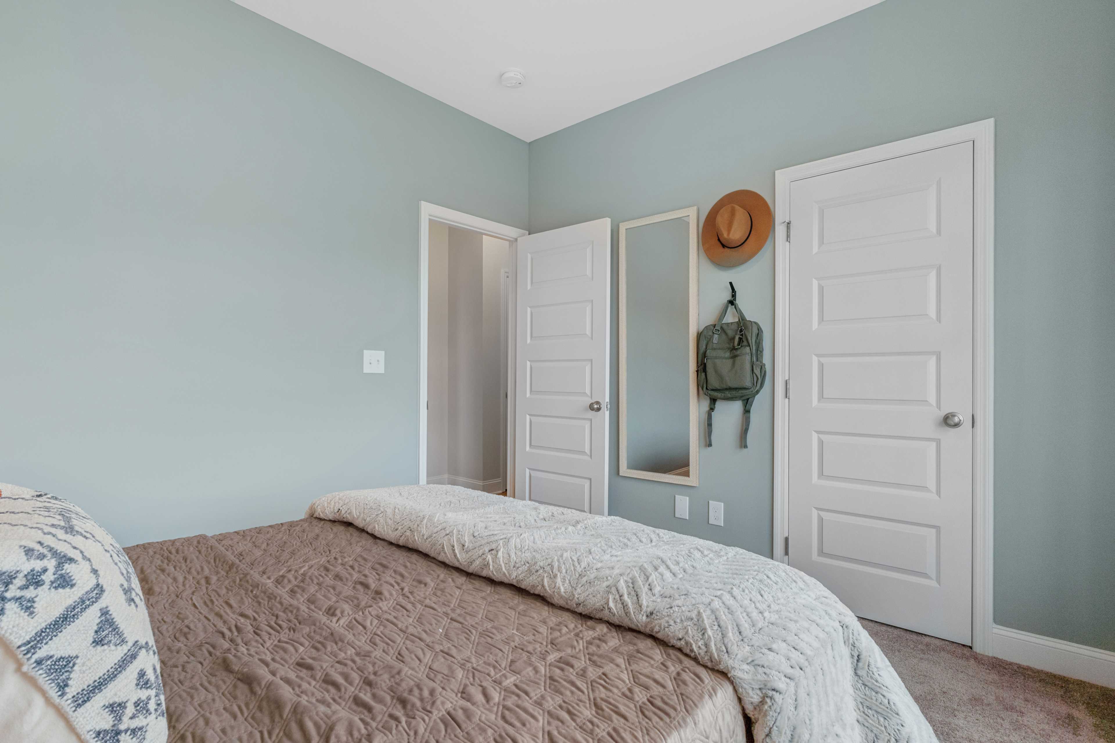 Light blue bedroom at The Retreat at Cain Park in Hartselle AL with queen bed, white floral bedding, mirrored closet doors, hanging hat and backpack