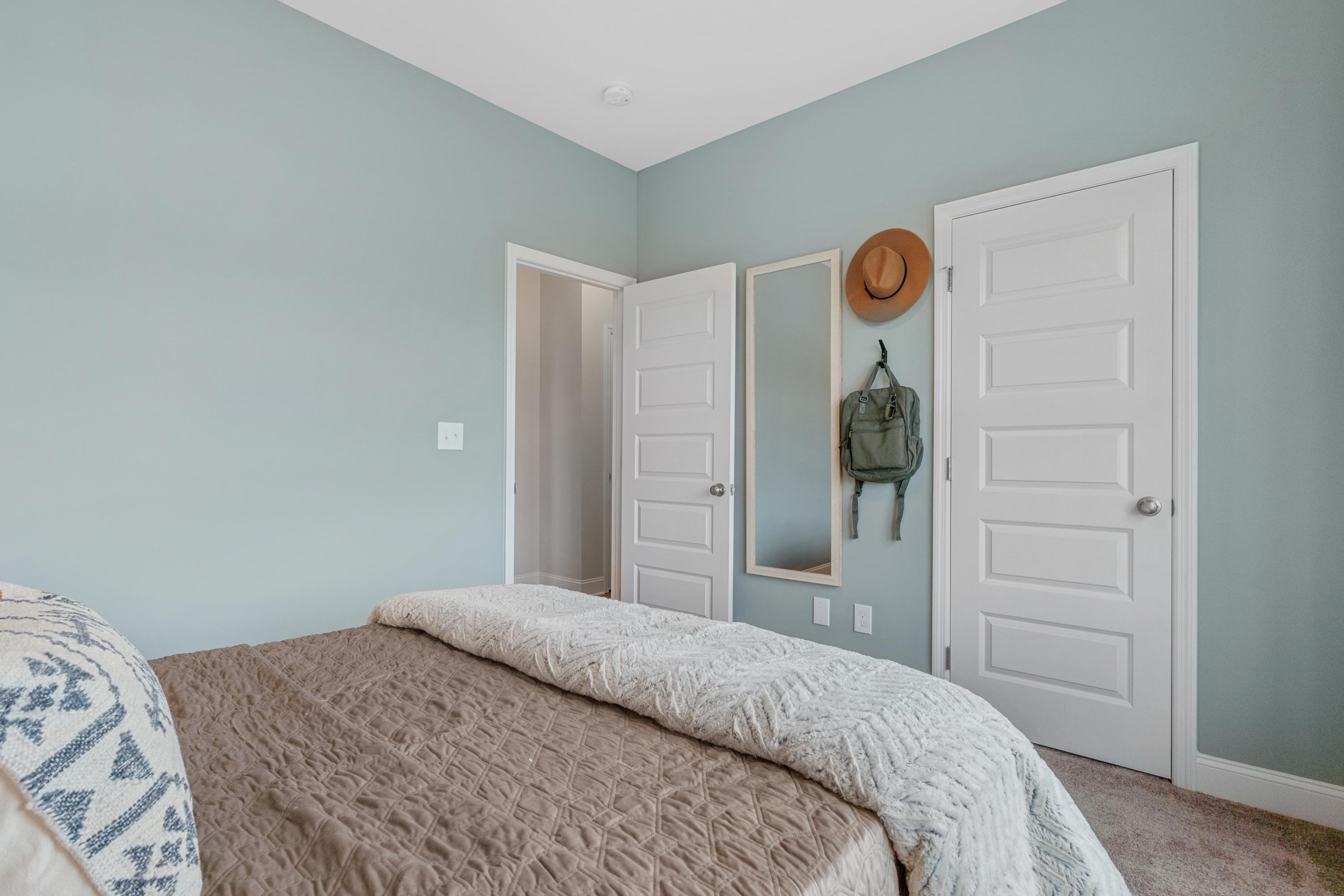 Light blue bedroom at The Retreat at Cain Park in Hartselle AL with queen bed, white floral bedding, mirrored closet doors, hanging hat and backpack