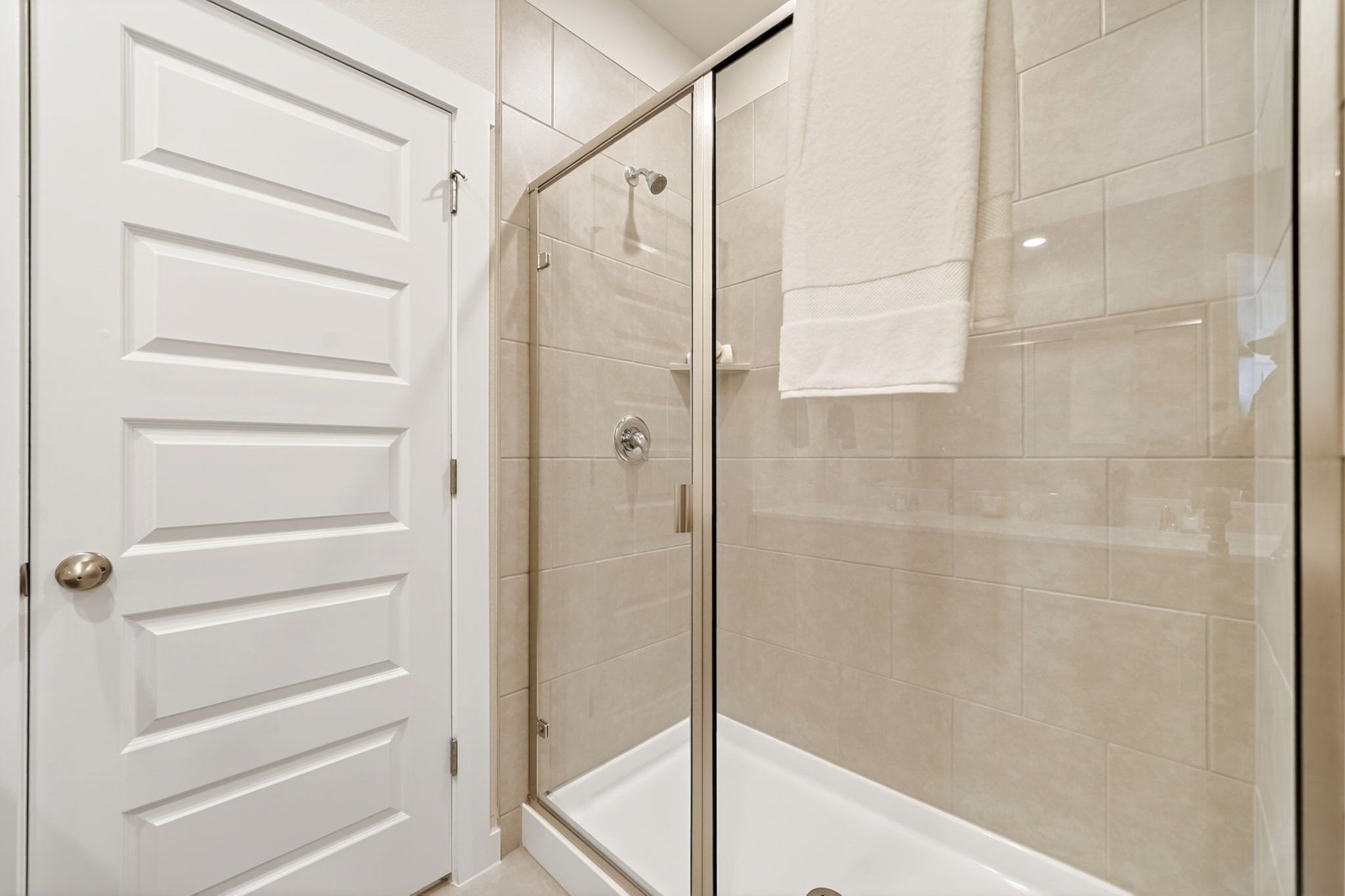 Modern glass shower with beige subway tiles and hanging towel in Heartland Texas bathroom by Davidson Homes