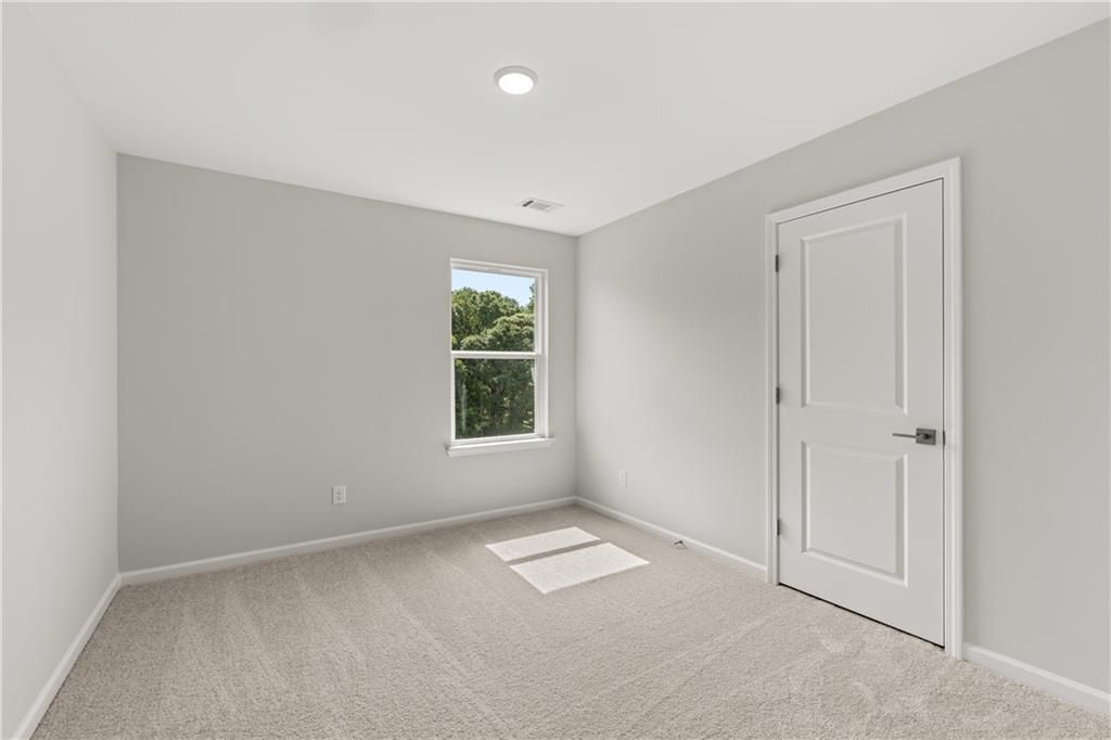 Bright secondary bedroom with plush carpet and neutral walls in The Russell A floor plan at Cedar Farms, Winder, Georgia.