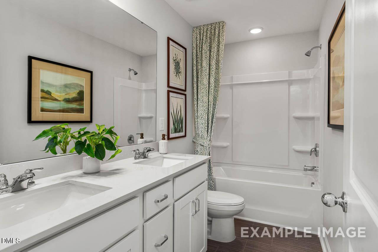 Modern bathroom with double vanity sinks, white cabinets, green shower curtain, and framed botanical art in Davidson Homes The Graham, Fuquay-Varina