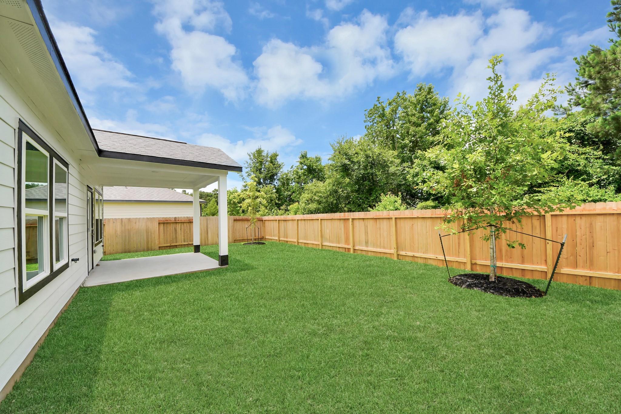 Covered patio and grassy backyard with wood privacy fence at The Blanco E home in Caney Creek Place, Conroe, Texas.