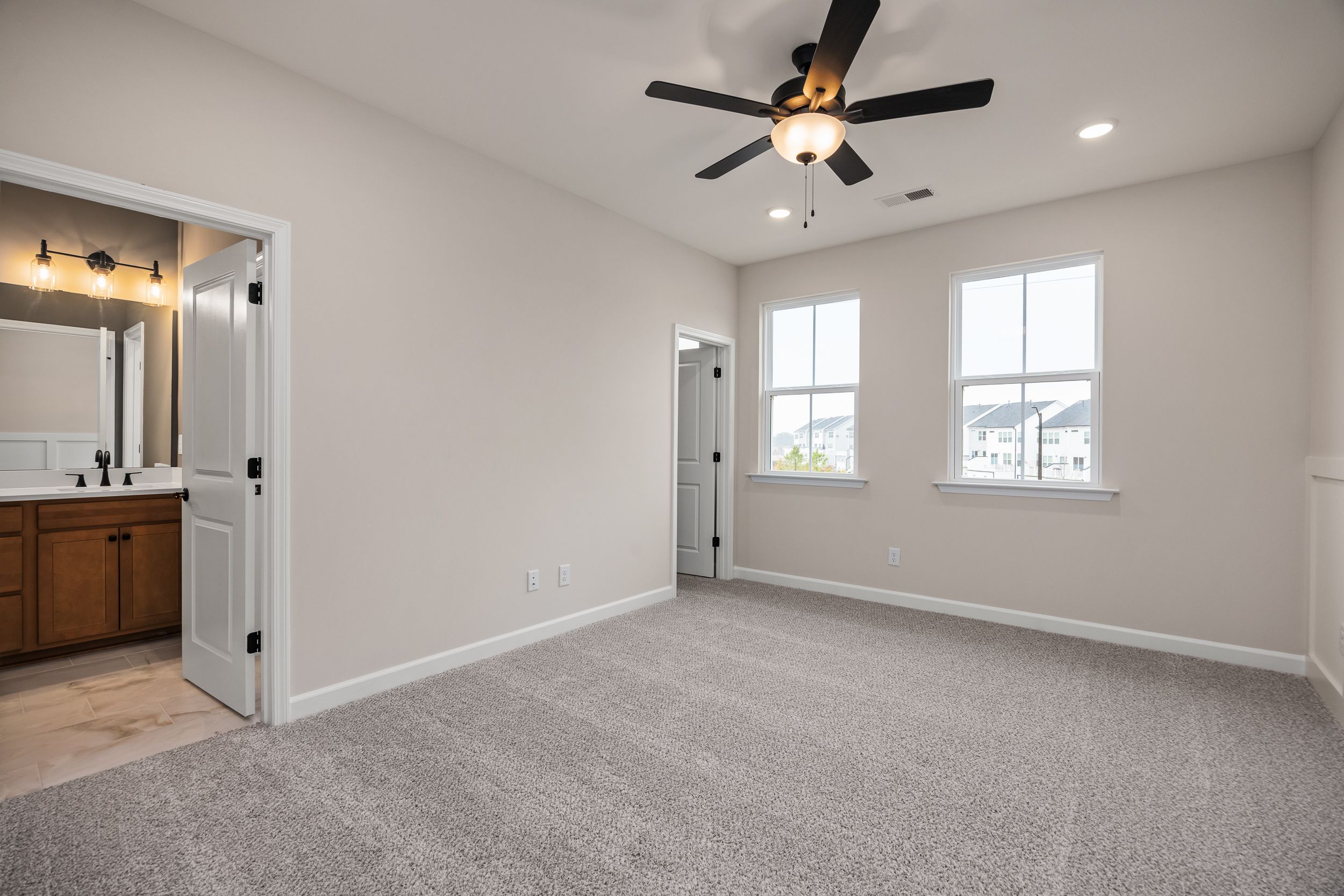 Spacious master bedroom with en-suite bathroom at Forestville Yard in Knightdale NC by Davidson Homes, beige walls, carpet, ceiling fan, large windows