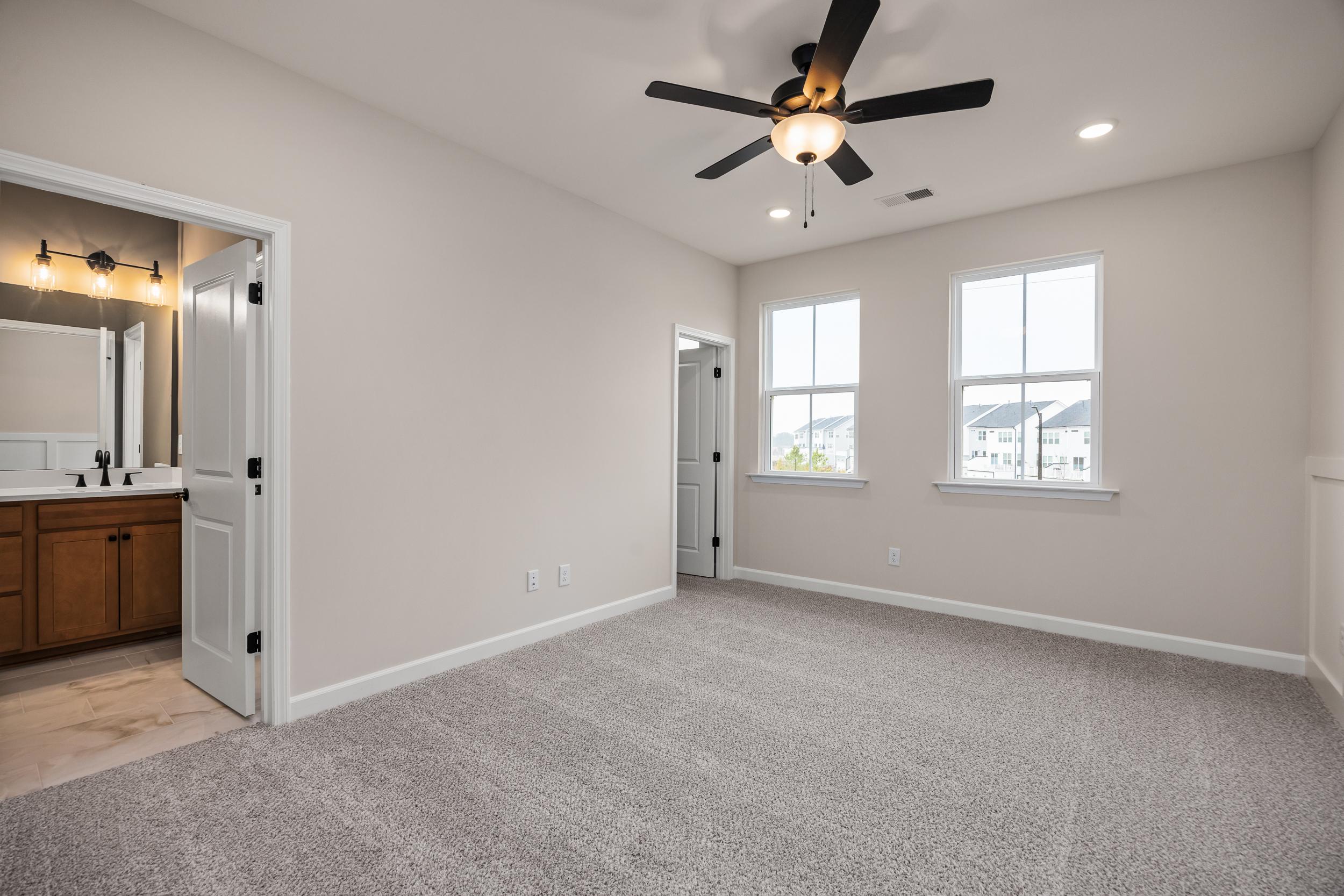 Spacious master bedroom with en-suite bathroom at Forestville Yard in Knightdale NC by Davidson Homes, beige walls, carpet, ceiling fan, large windows