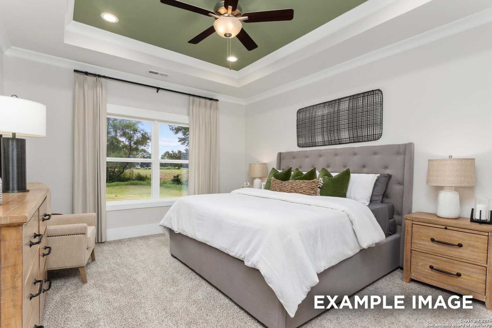 Cozy bedroom with green tray ceiling, ceiling fan, gray upholstered bed, and large window to lush yard in Davidson Homes The Daphne H, Seguin, Texas