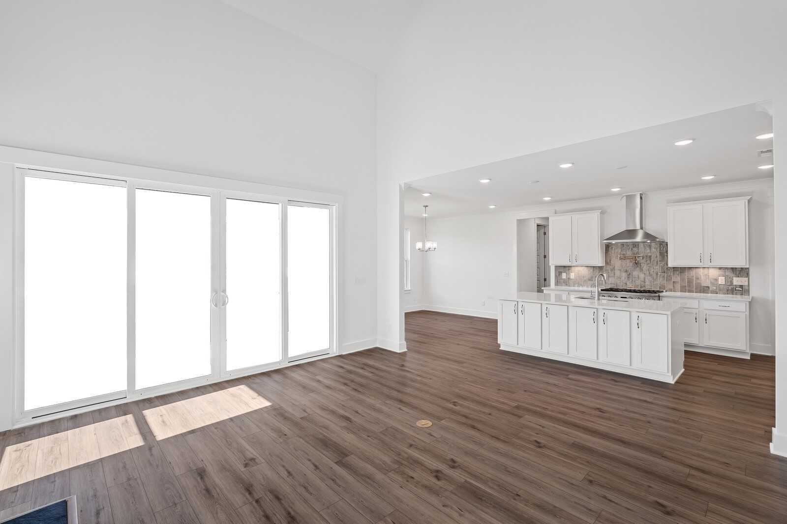 Bright open-concept great room with hardwood floors, large sliding doors, and modern white kitchen island in Davidson Homes The Hawkins, Murfreesboro