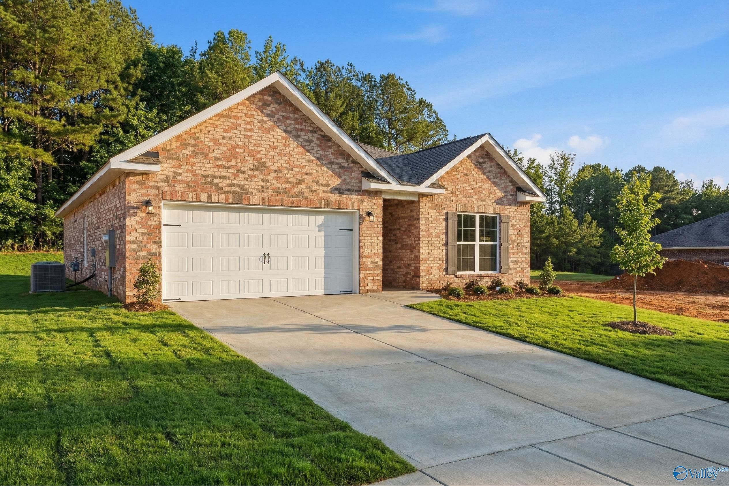 Brick single-story home with 2-car garage, concrete driveway, lush green lawn, and trees in The Highlands, Arab, Alabama