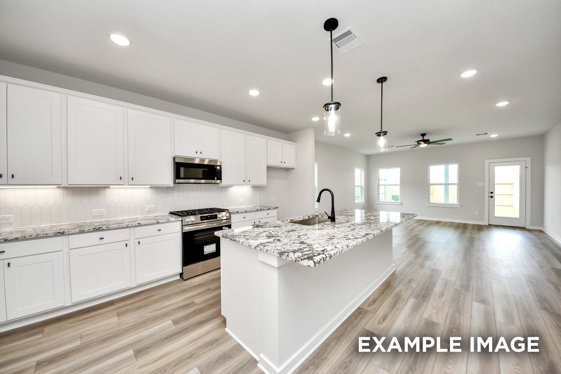 Modern open-concept kitchen in The Sorrento with white cabinetry, granite island, and stainless steel appliances.
