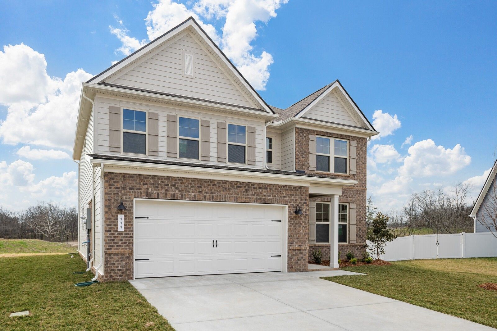 Two-story beige brick home with two-car garage, front yard landscaping in Woods Crossing, Gallatin, Tennessee by Davidson Homes