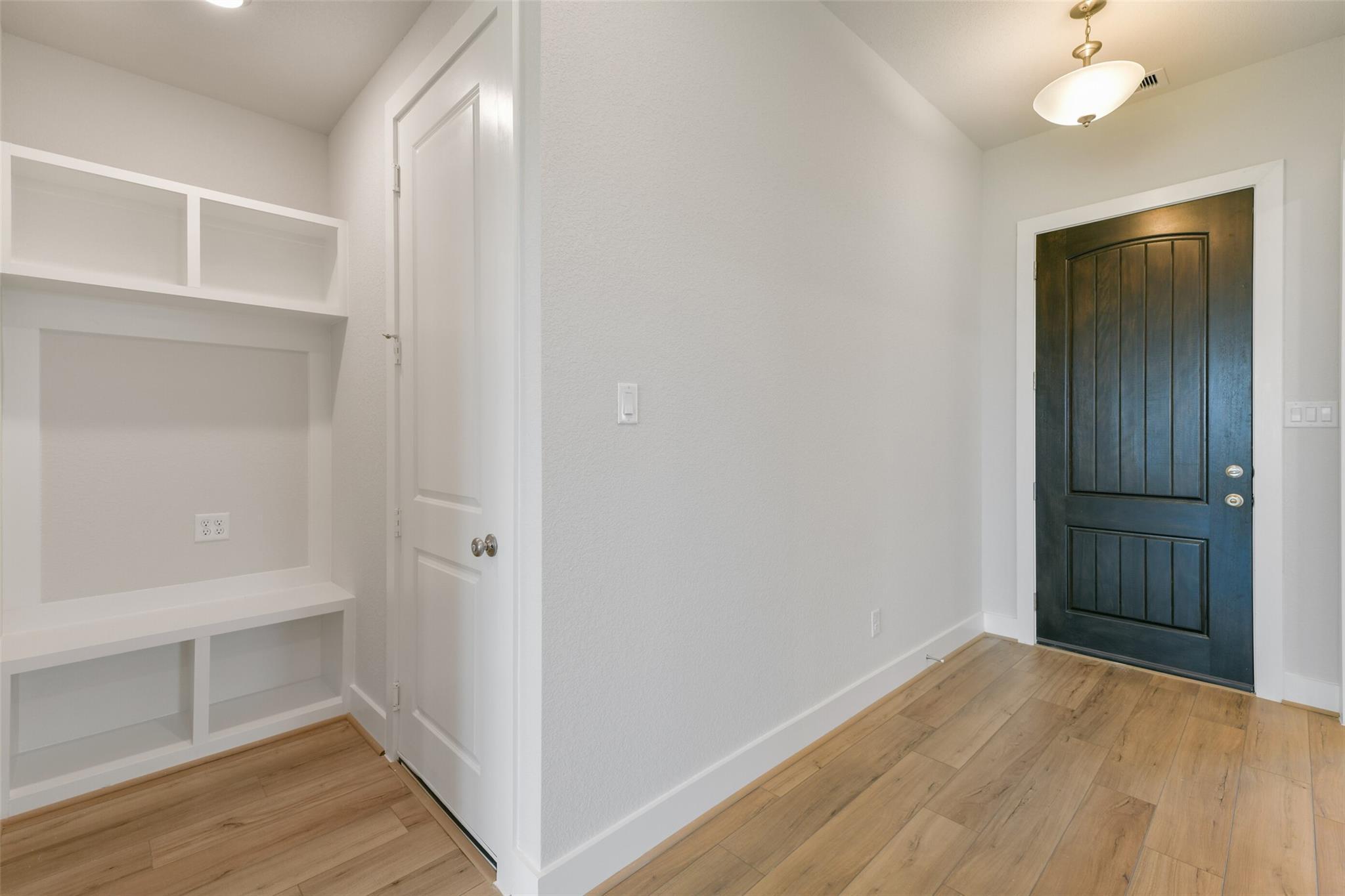 Built-in white mudroom lockers and benches with wood flooring in hallway of Davidson Homes The Edward A, Lago Mar, Texas City