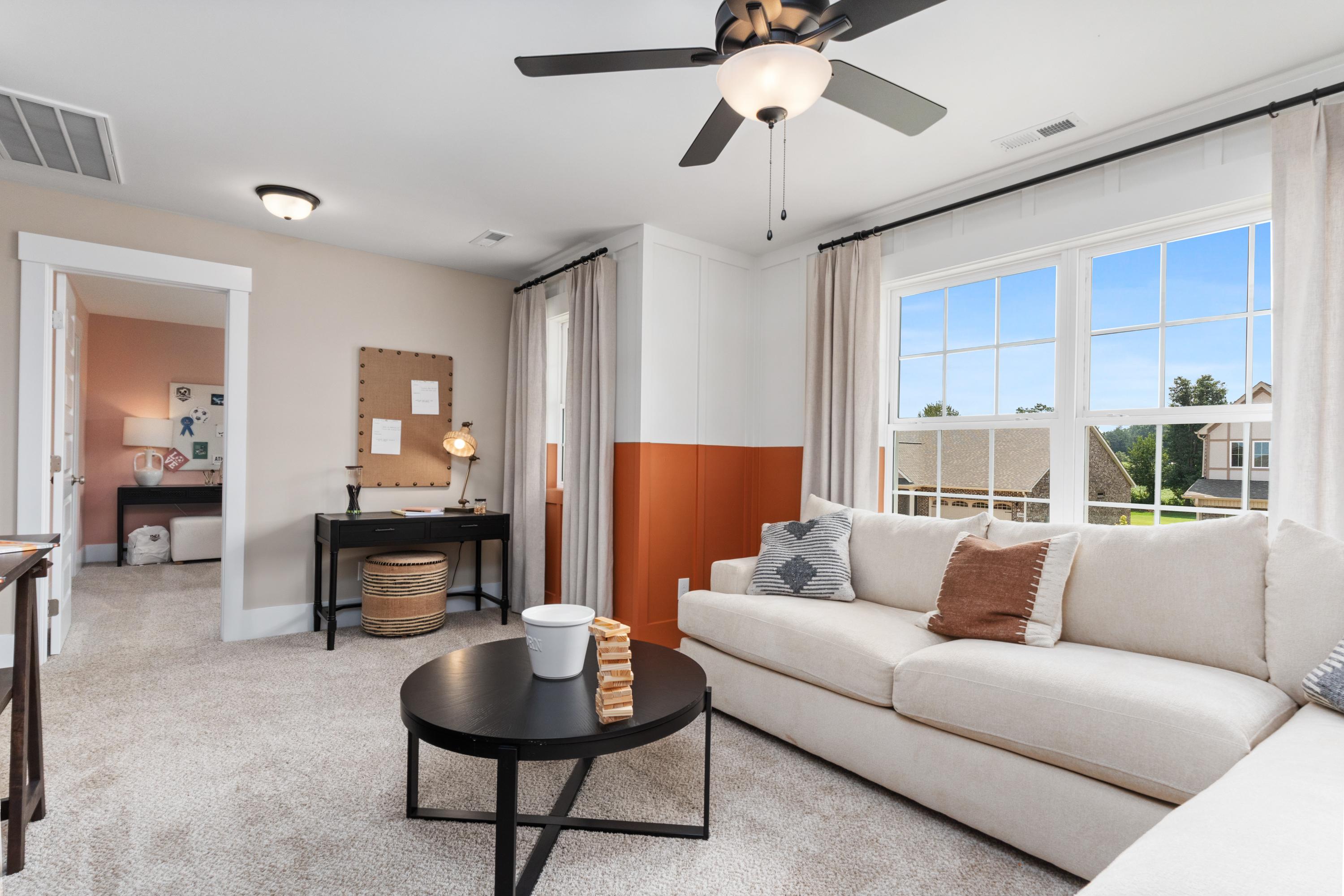 Cozy living room in The Shelby A home with beige sofa, orange accent wall, built-in desk, and large windows