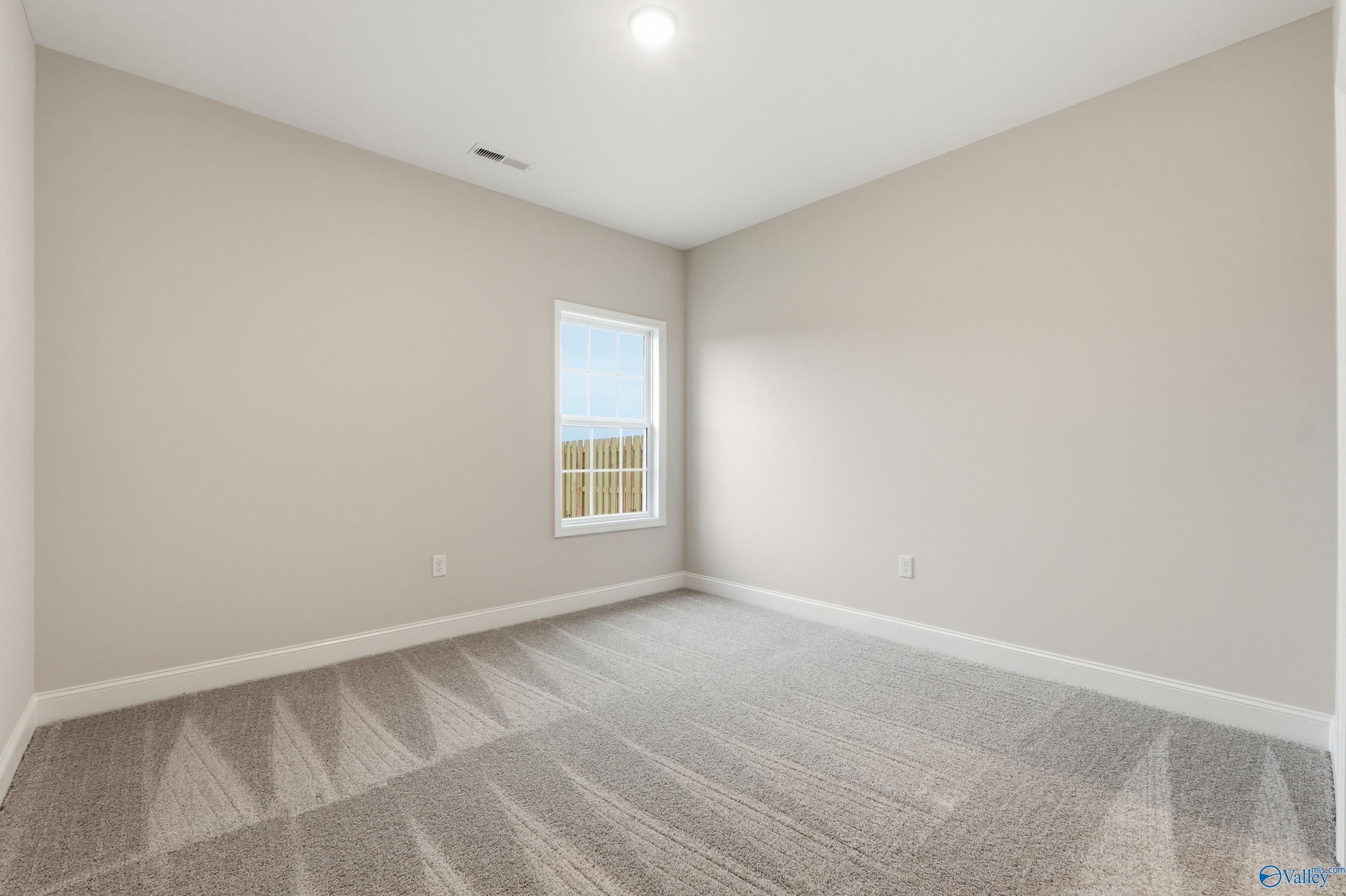Bright secondary bedroom with beige walls, plush carpet, and large window in Davidson Homes The Kirkland, Decatur, Alabama