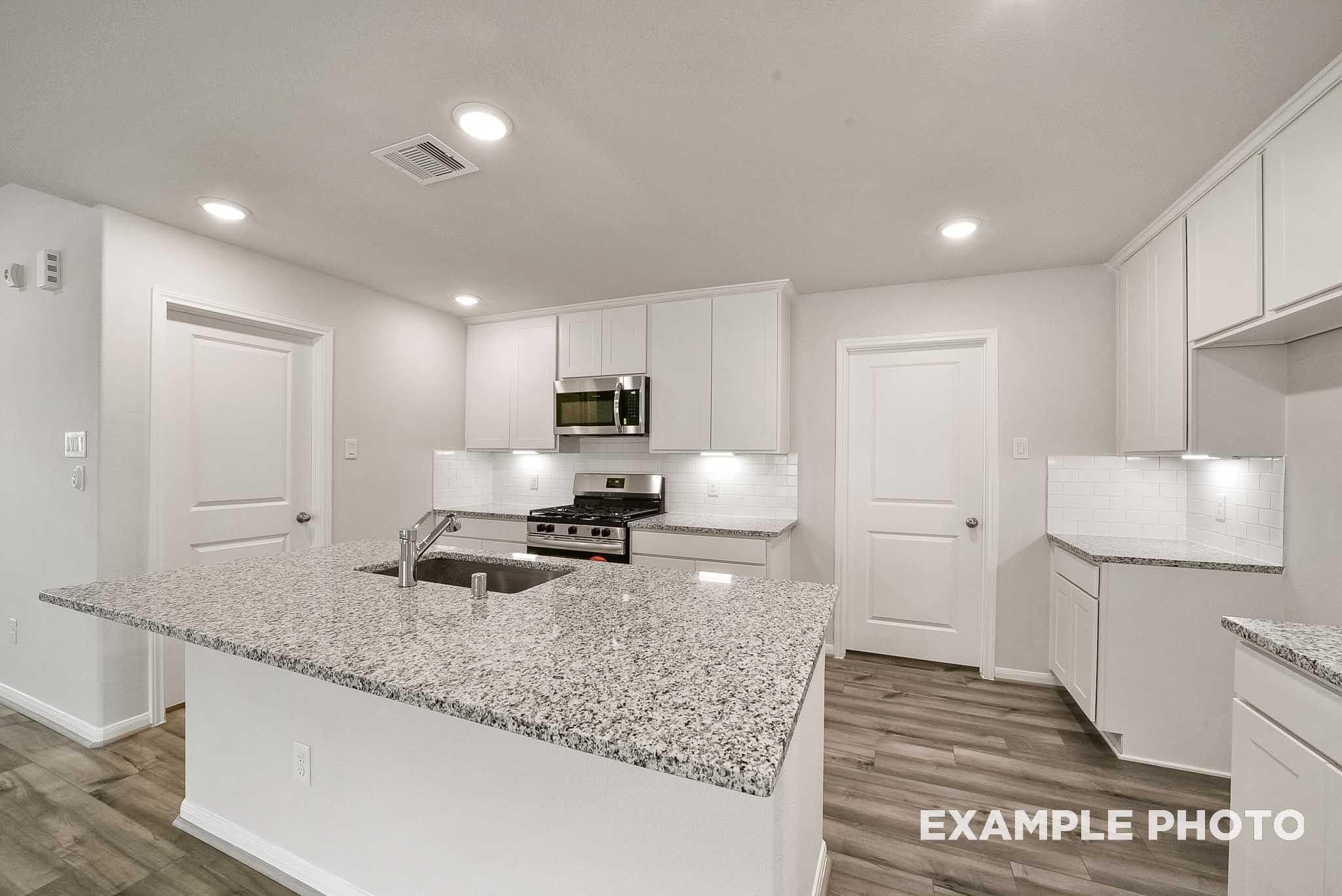 Modern kitchen with white cabinets, granite island, stainless appliances in Davidson Homes The Tierra B, Beasley, TX