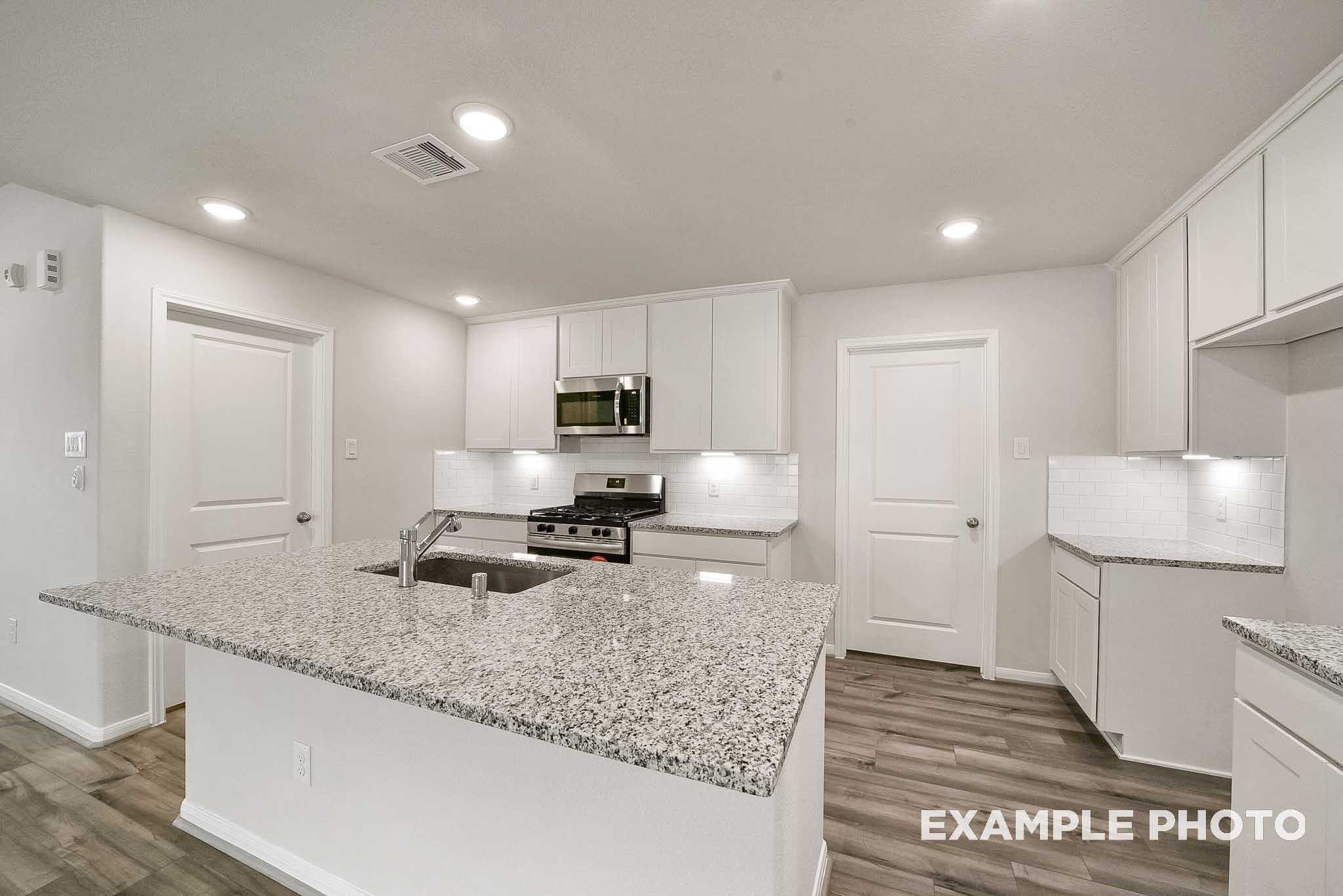 Modern kitchen with white cabinets, granite island, stainless appliances in Davidson Homes The Tierra B, Beasley, TX