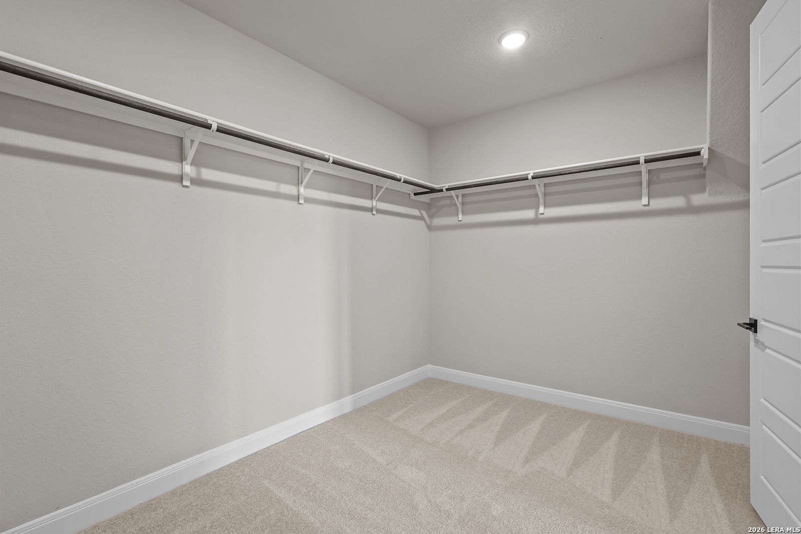 Spacious walk-in closet with corner hanging rods and neutral carpet in Davidson Homes The Foster E, Potranco Oaks, Castroville, TX