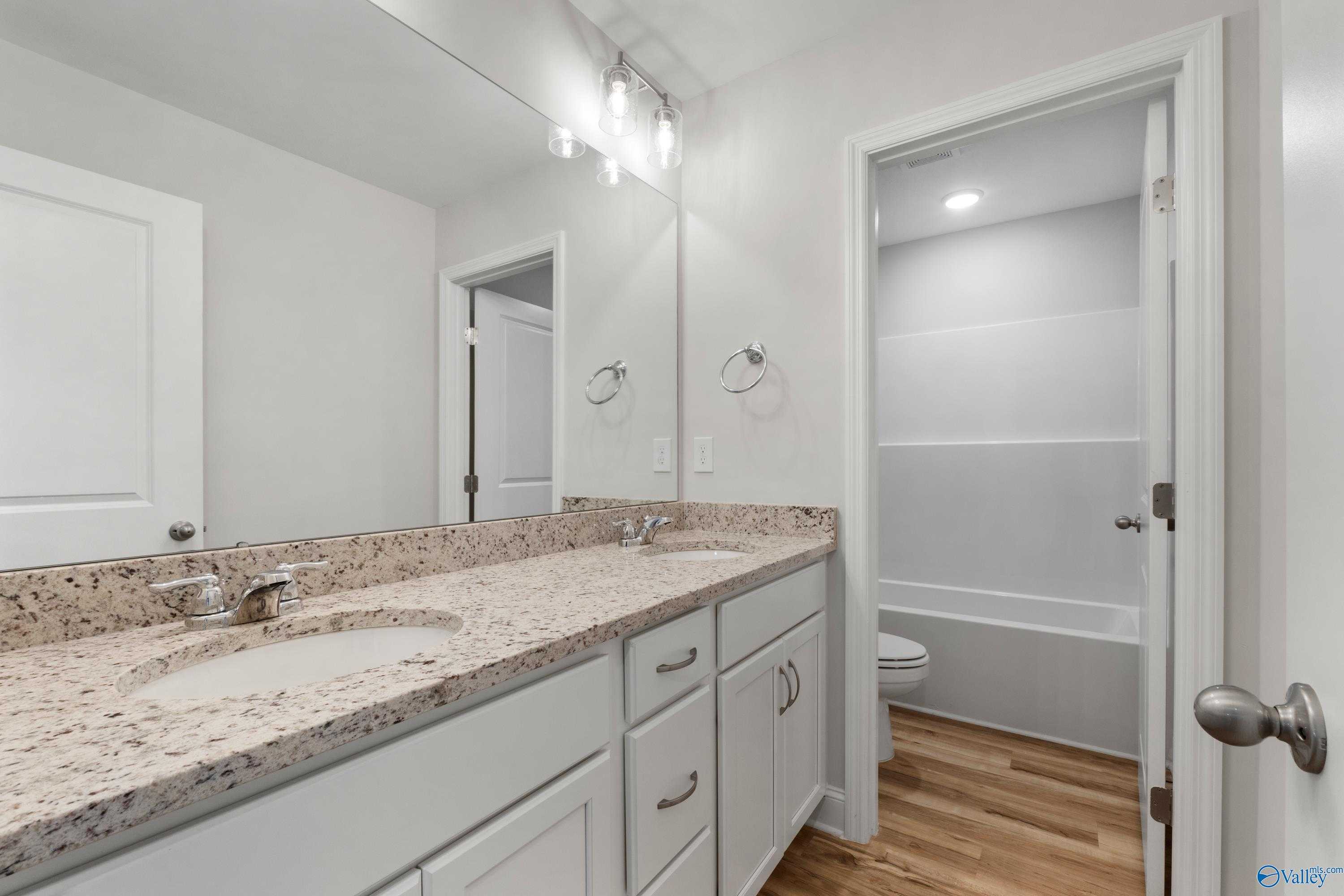 Modern double vanity bathroom with granite countertops, white cabinets, and hardwood floors in Davidson Homes The Chelsea C, Harvest, Alabama