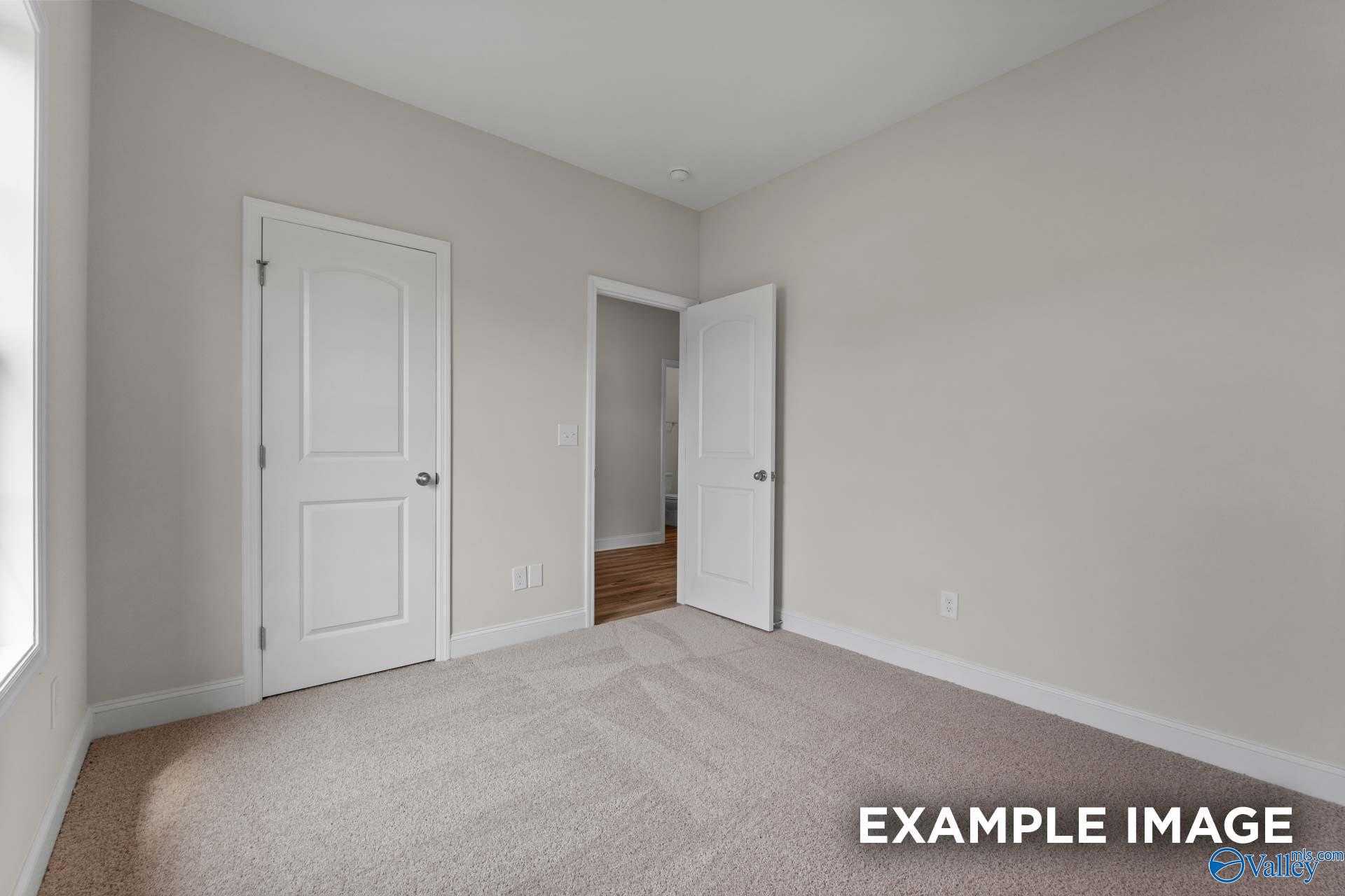 Spacious secondary bedroom with neutral beige walls, carpeted floor, and open bathroom door in Davidson Homes The Butler plan, Toney, Alabama
