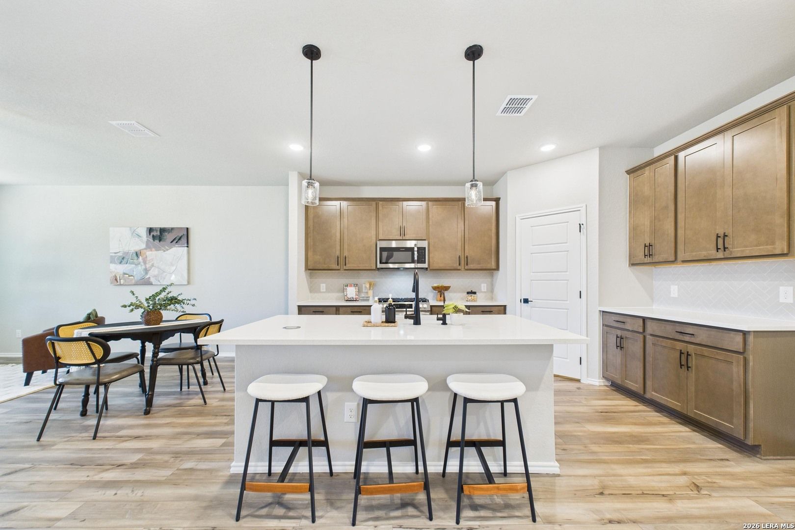 Open-concept kitchen with central island, granite counters, stainless appliances, and wood flooring in Davidson Homes Douglas E, Bricewood, San Antonio