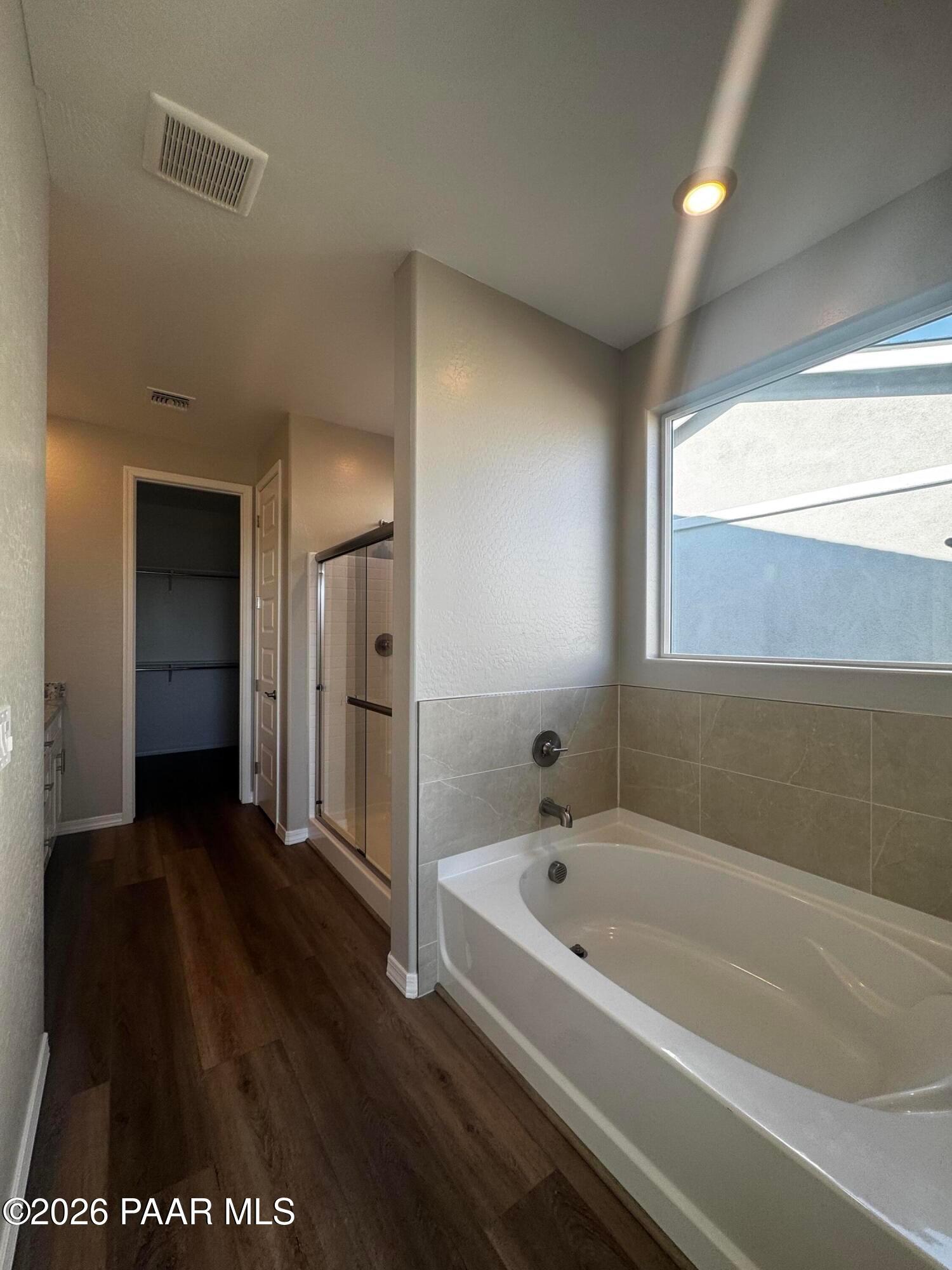 Modern master bathroom with deep soaking tub, glass shower, neutral tiles, and large window in Davidson Homes Daybreak B, Prescott AZ