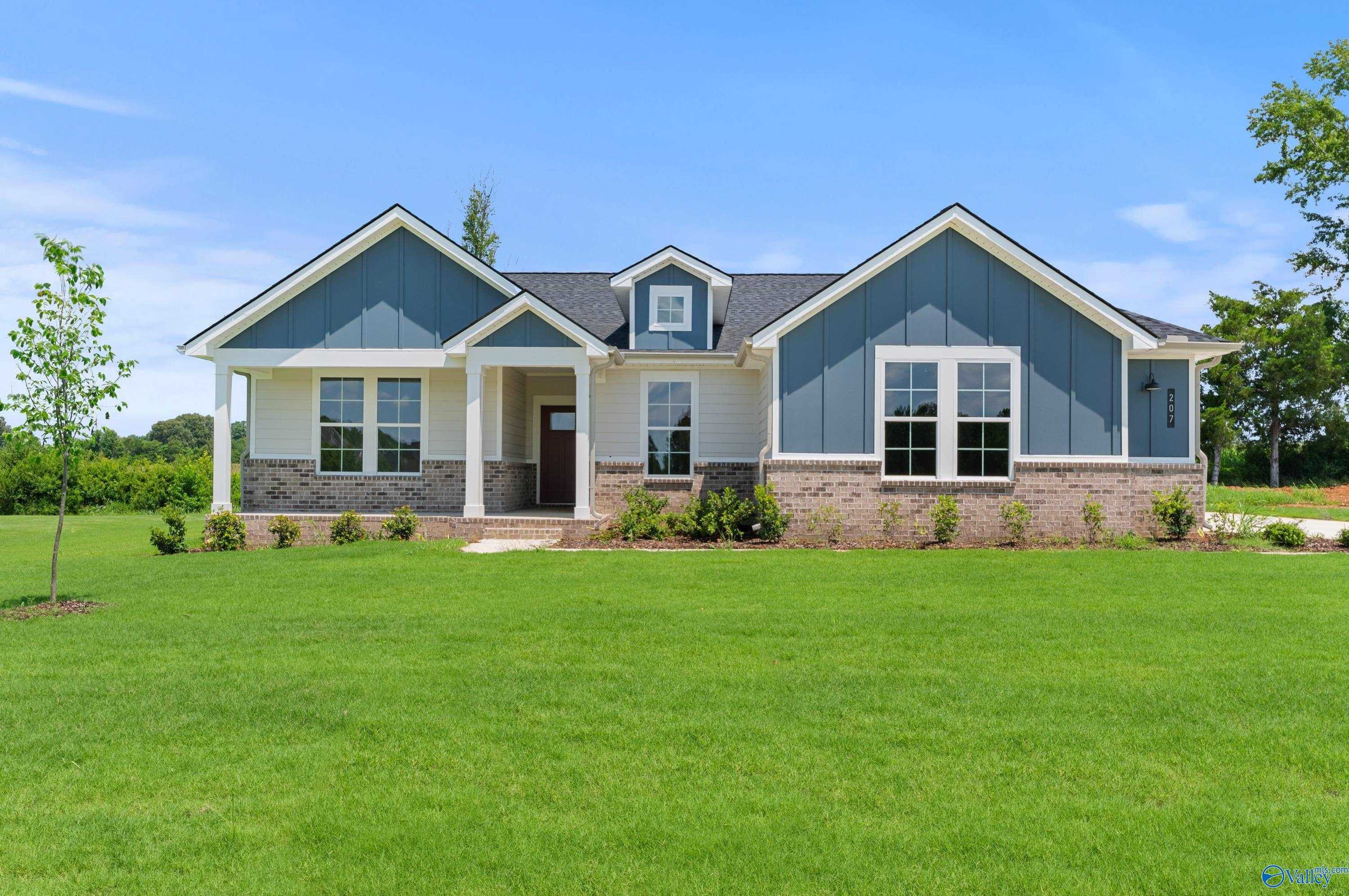 Modern blue single-story home with gabled roof, stone accents, front porch, and lush green lawn in Riverton Preserve, Huntsville