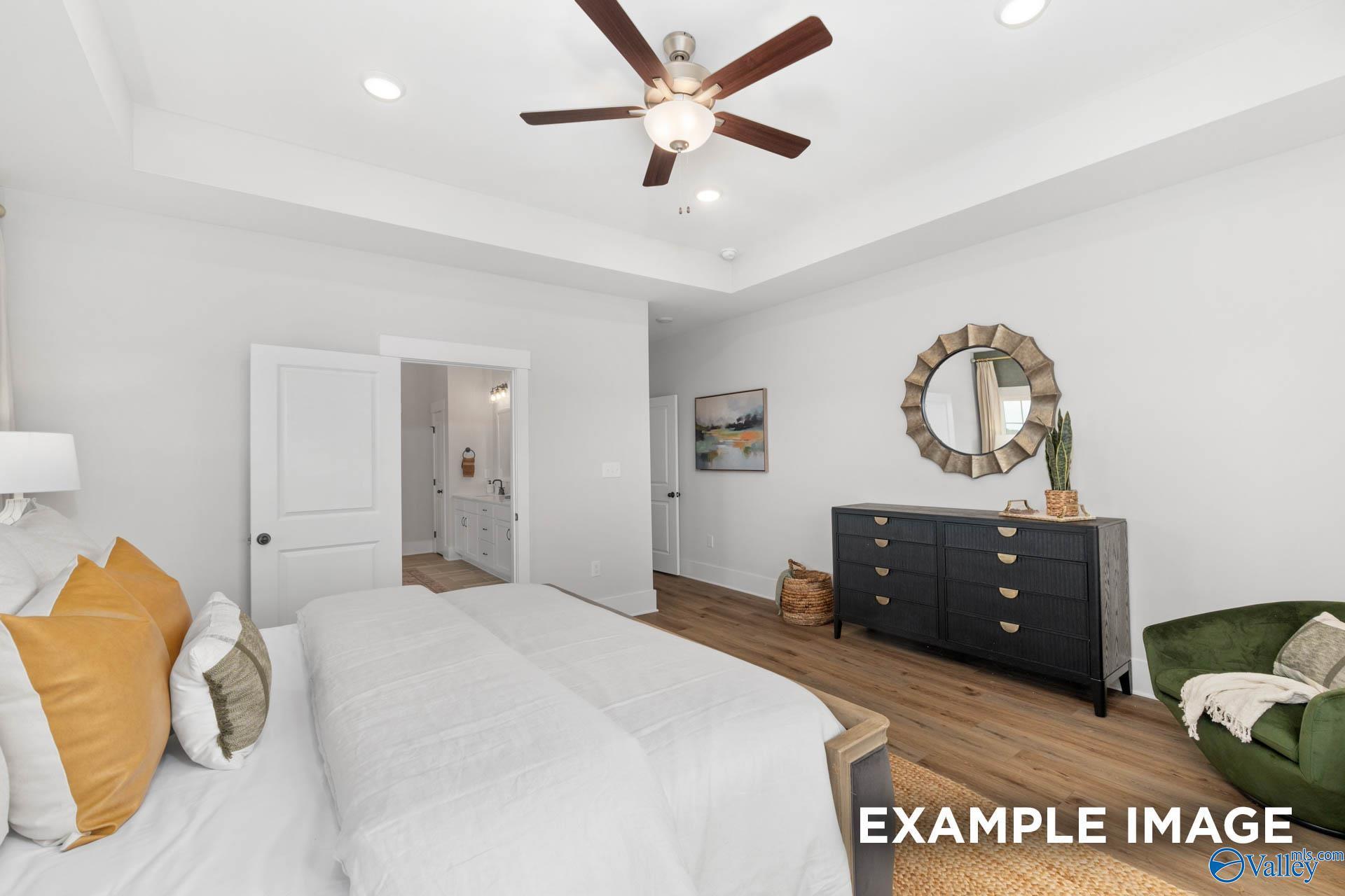 Elegant master bedroom with ceiling fan, white bedding, orange pillows, and open bathroom door in Davidson Homes The Finleigh, Decatur AL