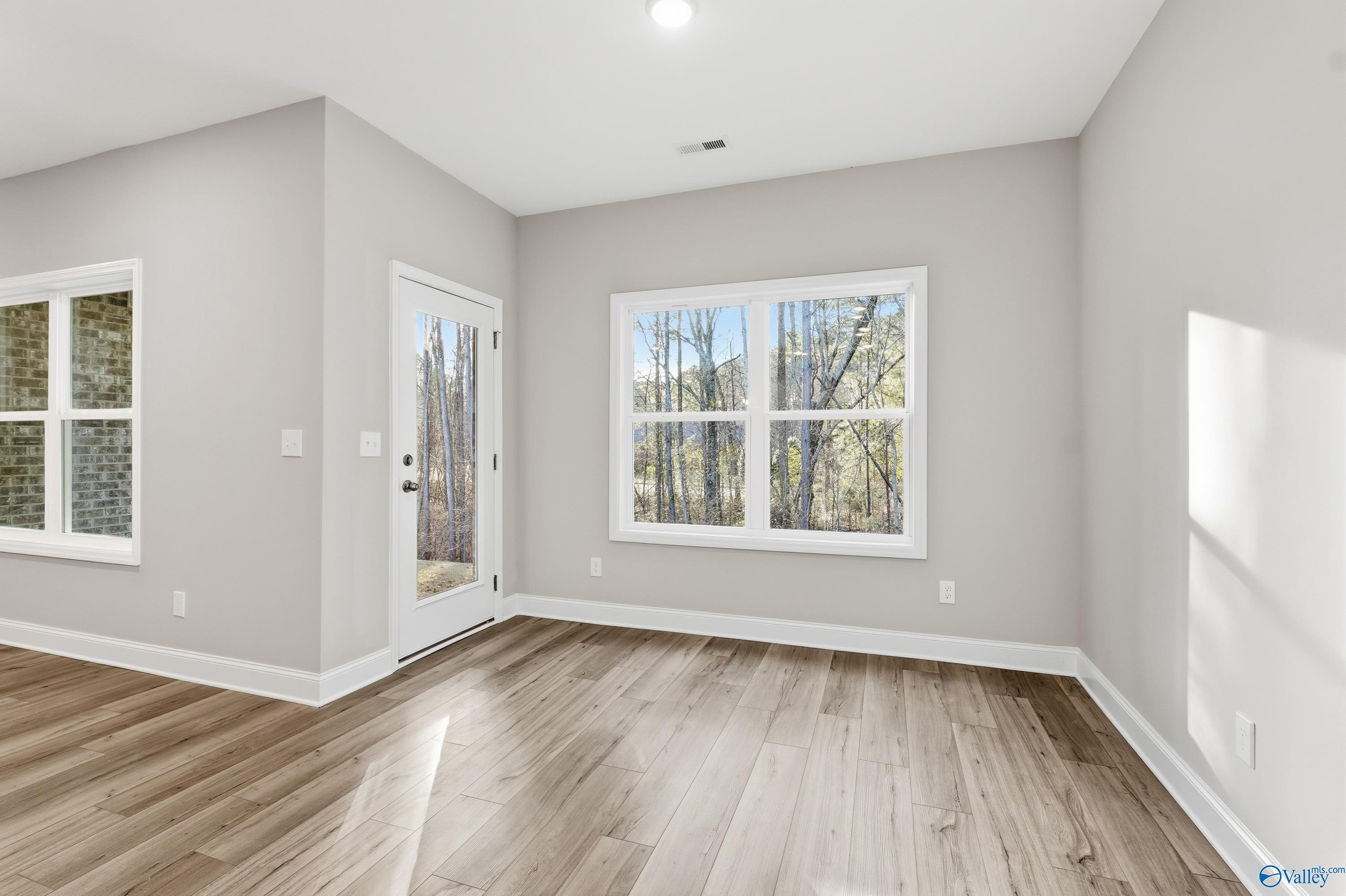 Bright living room with hardwood floors, gray walls, and large windows to wooded view in The Asheville by Davidson Homes, Arab, AL