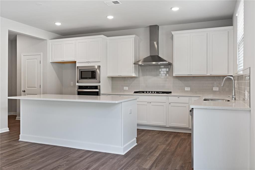 Modern white kitchen with stainless steel appliances, large island, subway tile backsplash in Davidson Homes The Hickory A, Winder, GA