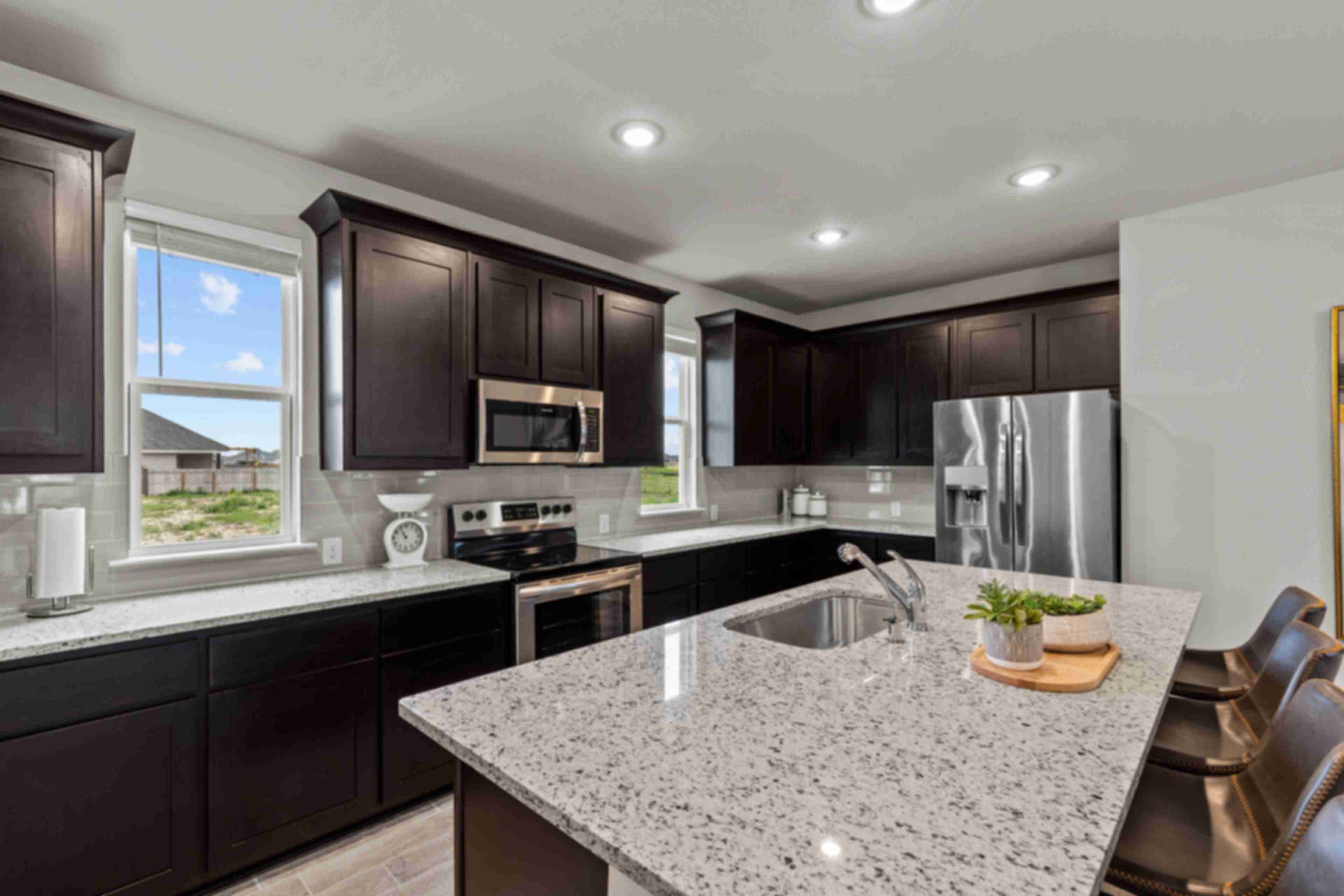 Modern kitchen in Agave San Antonio home by Davidson Homes featuring dark cabinets, granite island, stainless appliances and bar seating