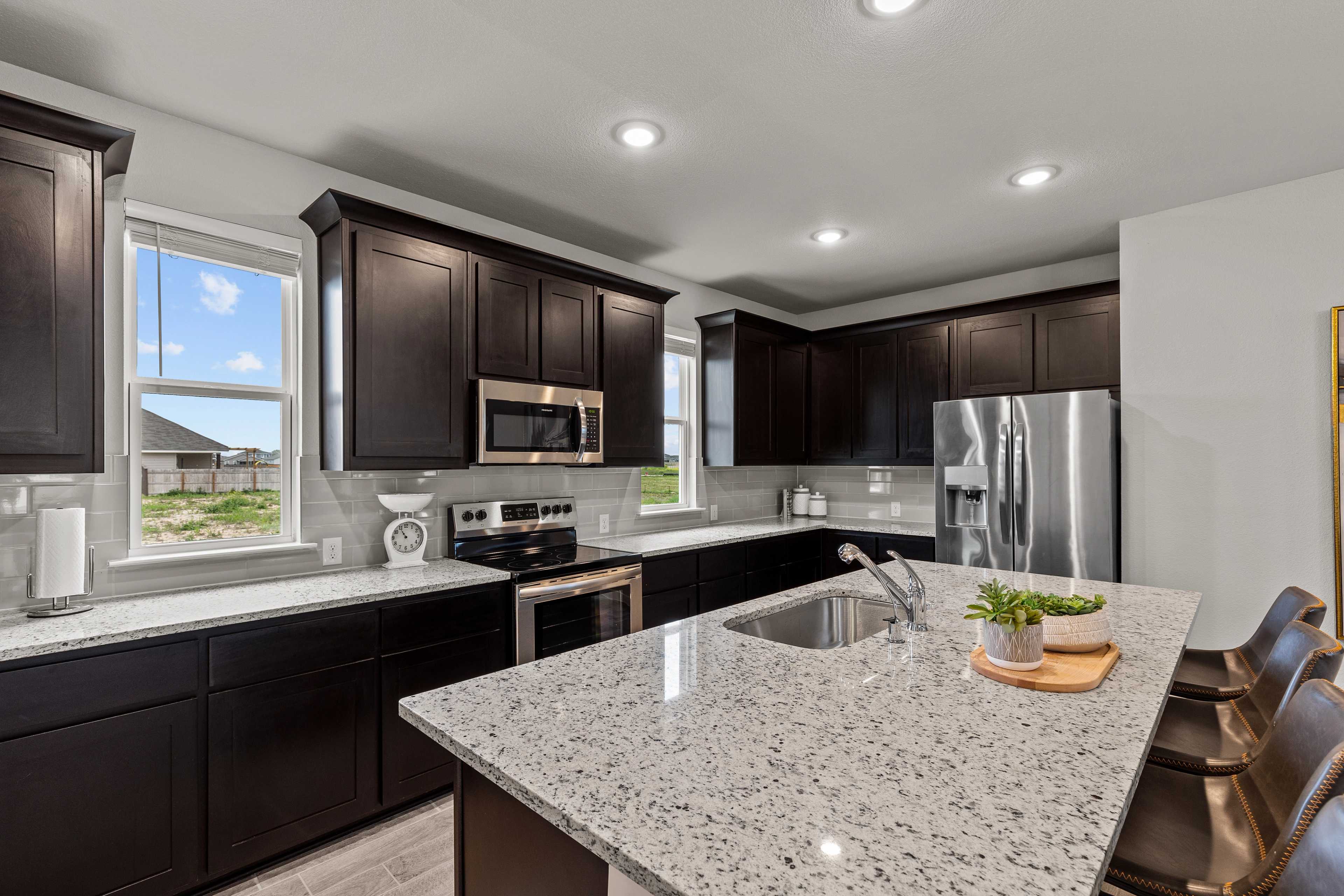 Modern kitchen with dark cabinets, granite island, stainless steel appliances at Hannah Heights in Seguin, Texas