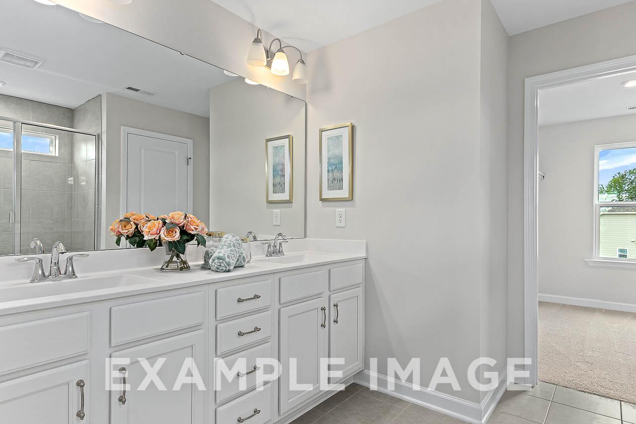 Spacious master bathroom in The Willow C featuring double white vanity, gray walls, orange roses, and frameless shower
