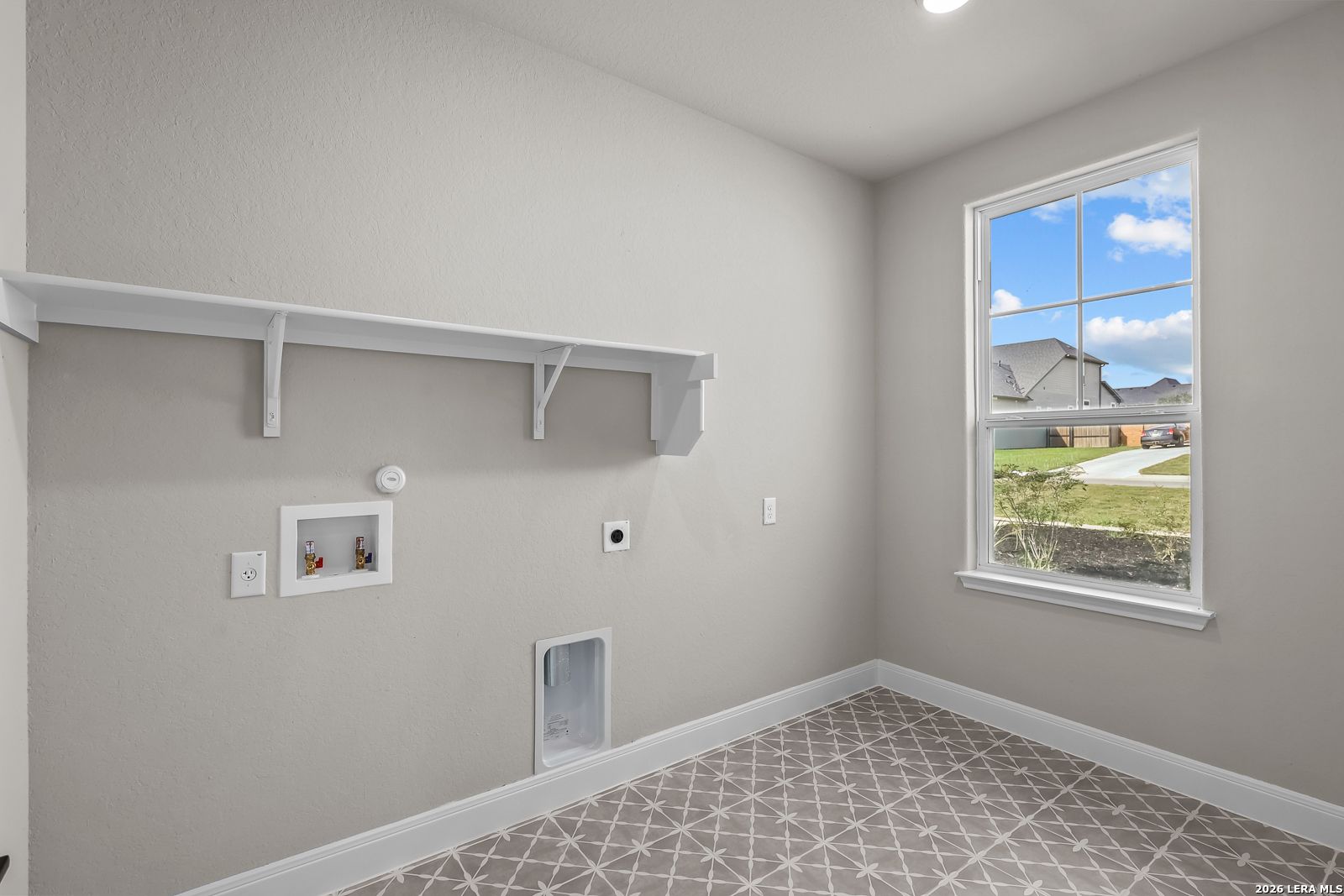 Bright laundry room with patterned tile floor, white shelving, and window in Davidson Homes Foster E plan, Castroville, TX