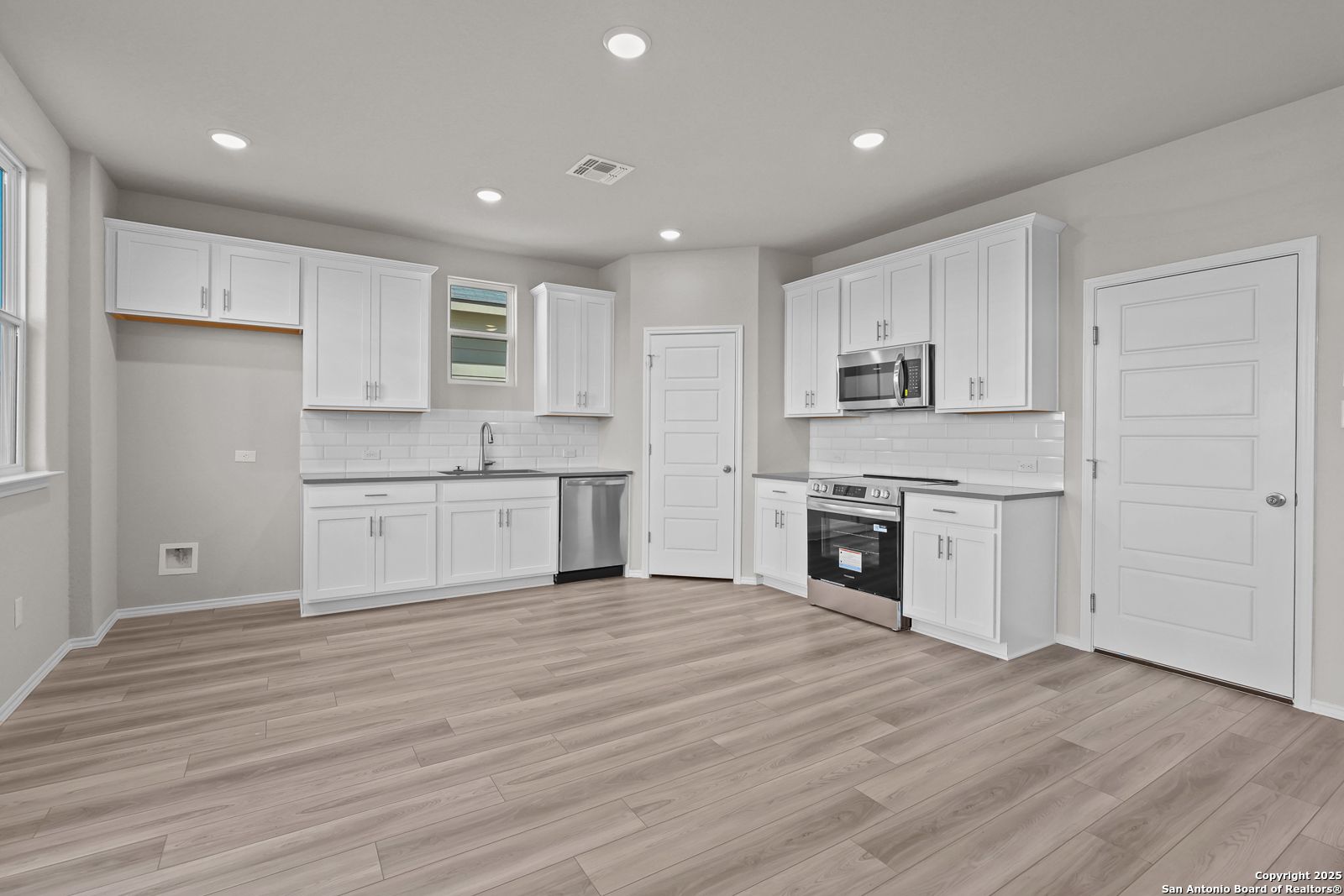 Modern white kitchen with stainless steel appliances, island sink, and open layout in Davidson Homes The Trinity D, San Antonio
