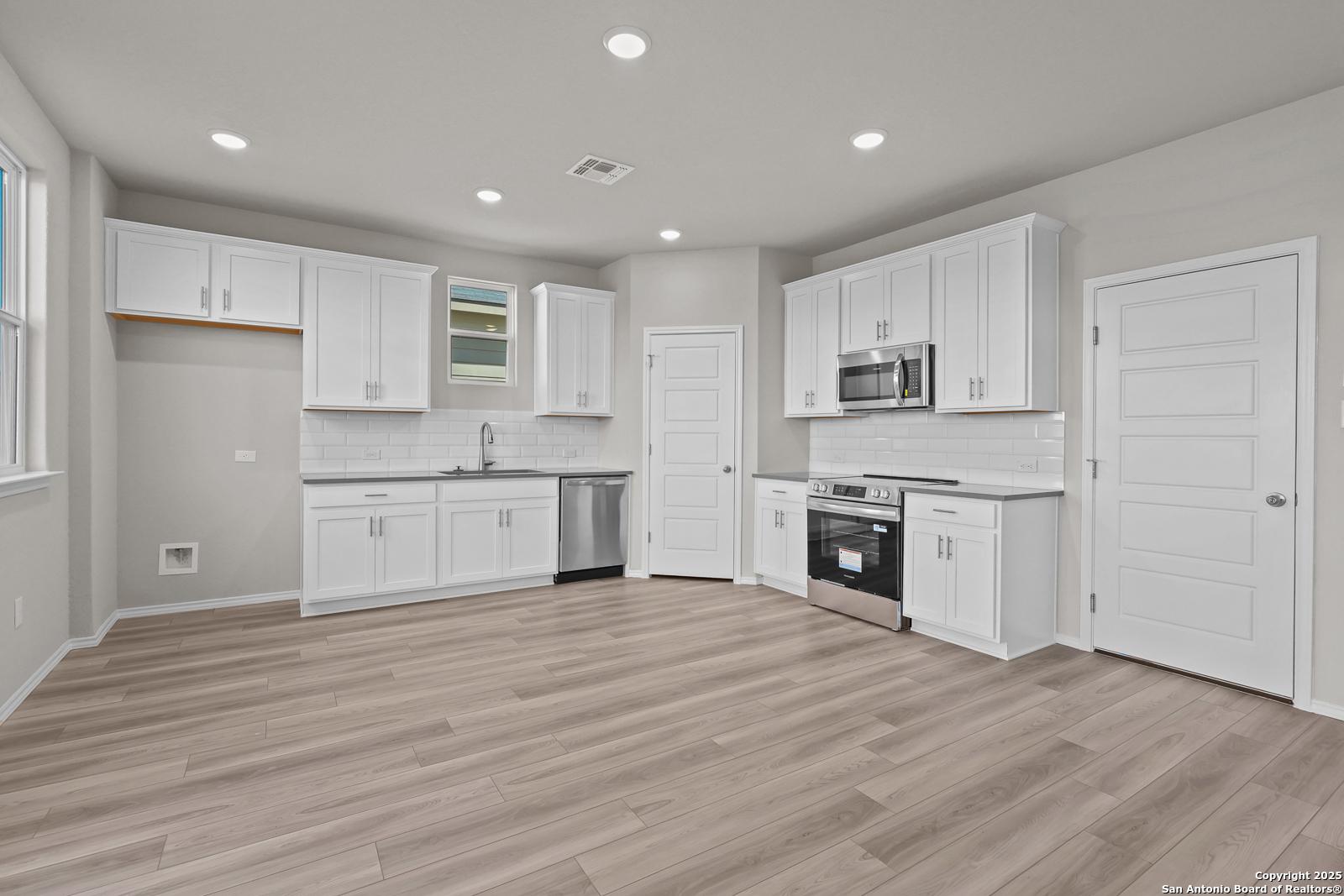 Modern white kitchen with stainless steel appliances, island sink, and open layout in Davidson Homes The Trinity D, San Antonio
