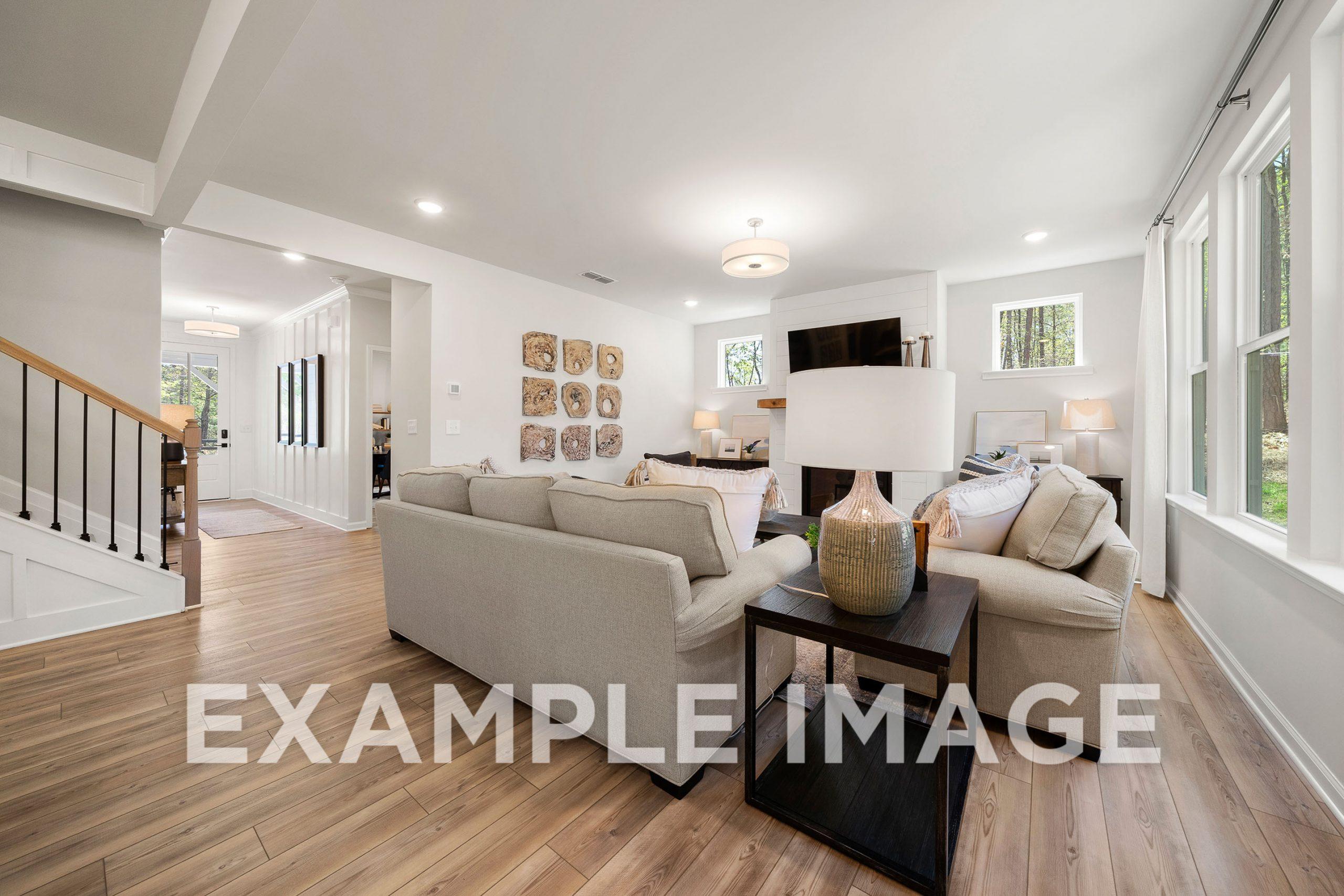 Spacious open-concept living room in The Hickory B with beige sofas, hardwood floors, large windows, and modern lighting